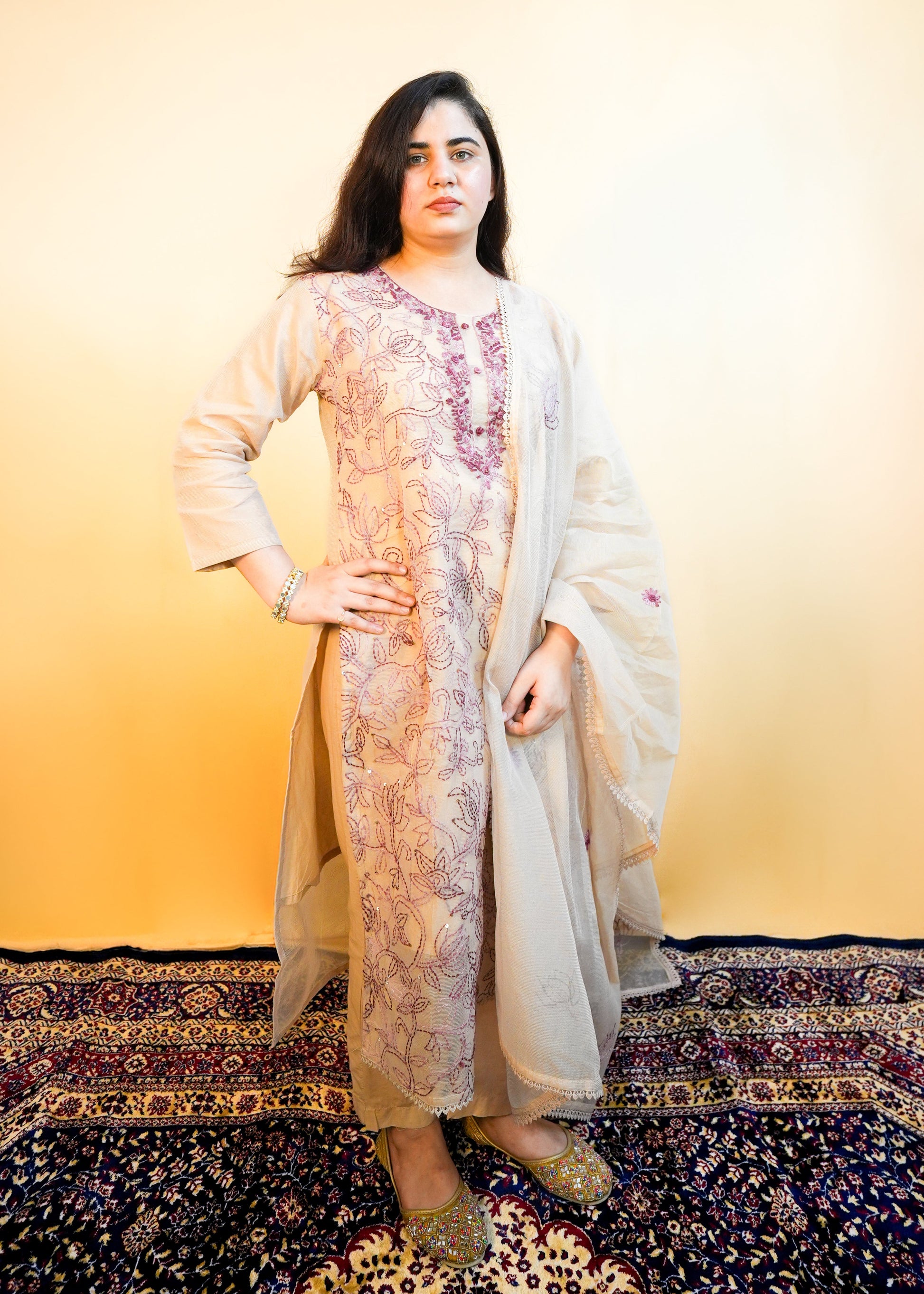 Woman in a traditional outfit standing on a patterned rug with a gradient yellow background