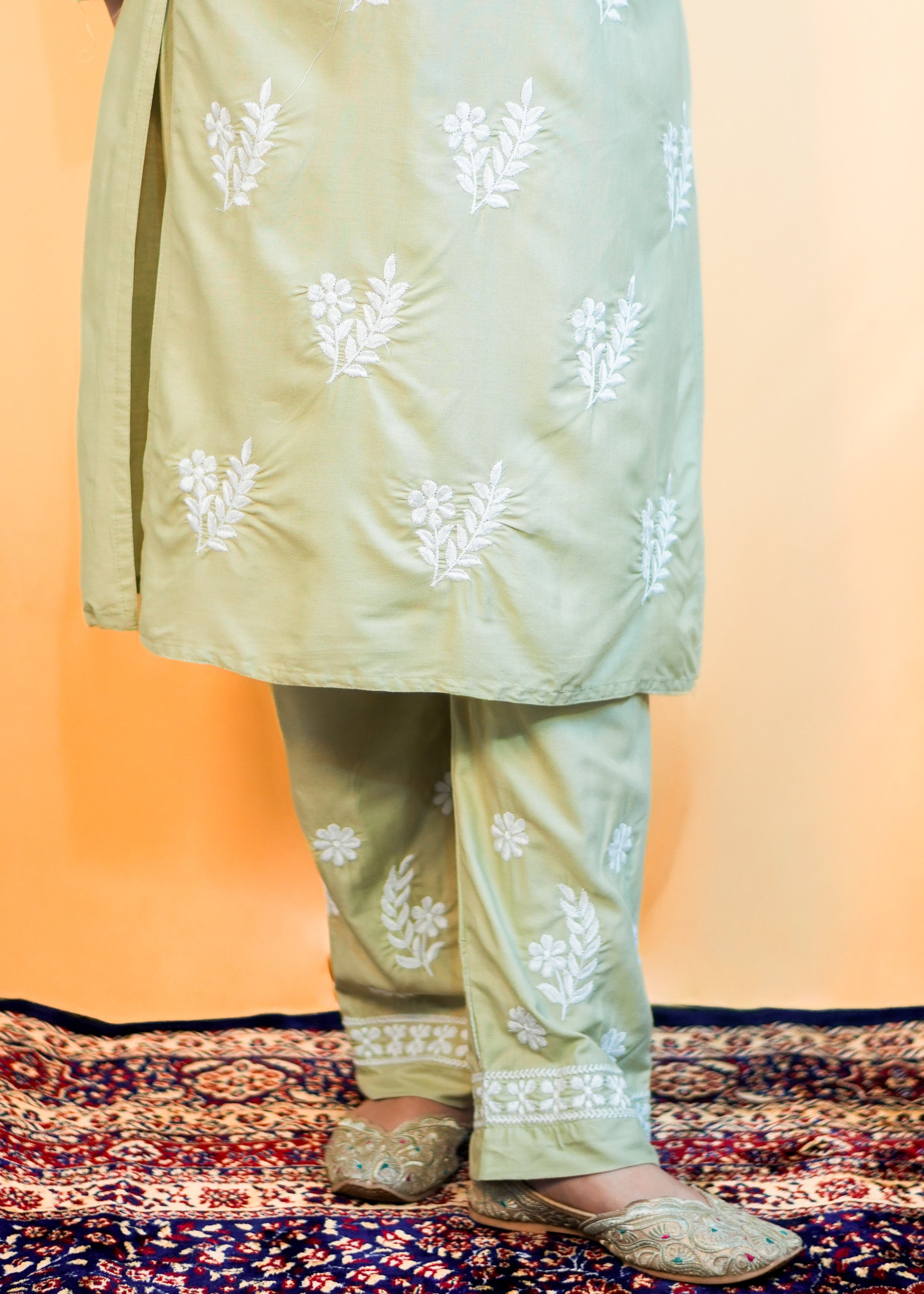 Light green traditional outfit with white floral patterns on a patterned rug.