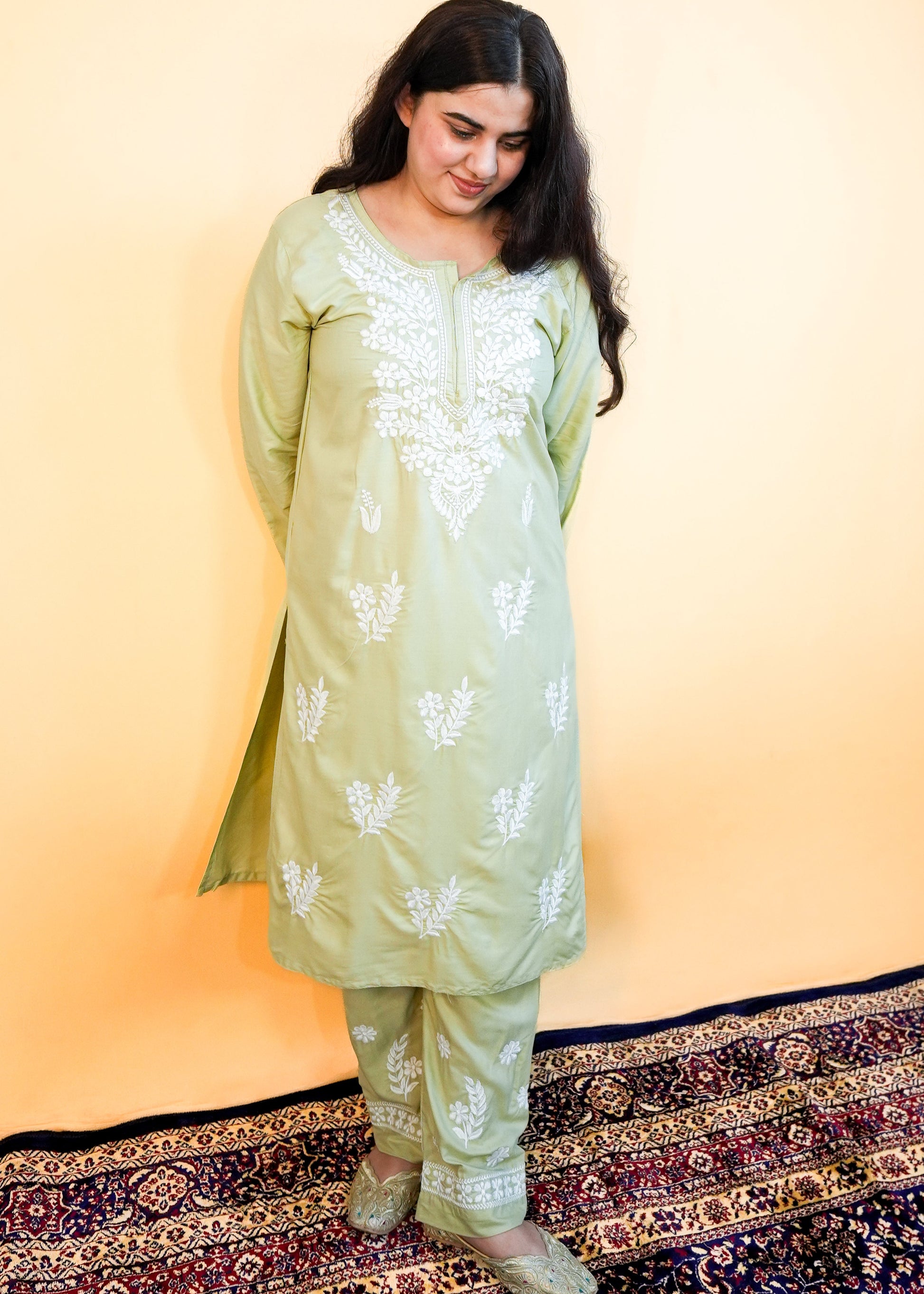 Woman wearing a light green traditional outfit with white patterns on a yellow background