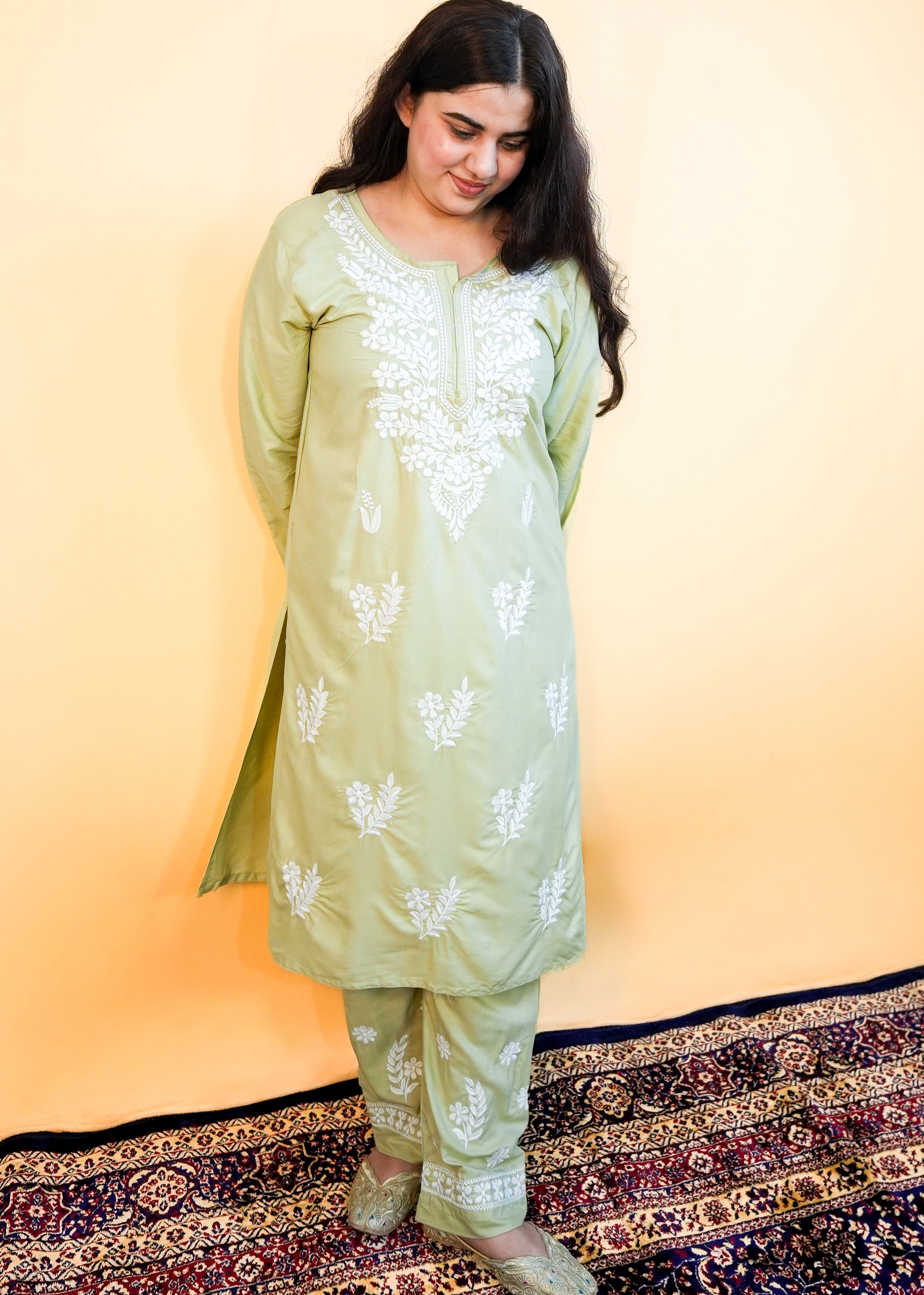 Woman wearing a light green traditional outfit with white patterns on a yellow background