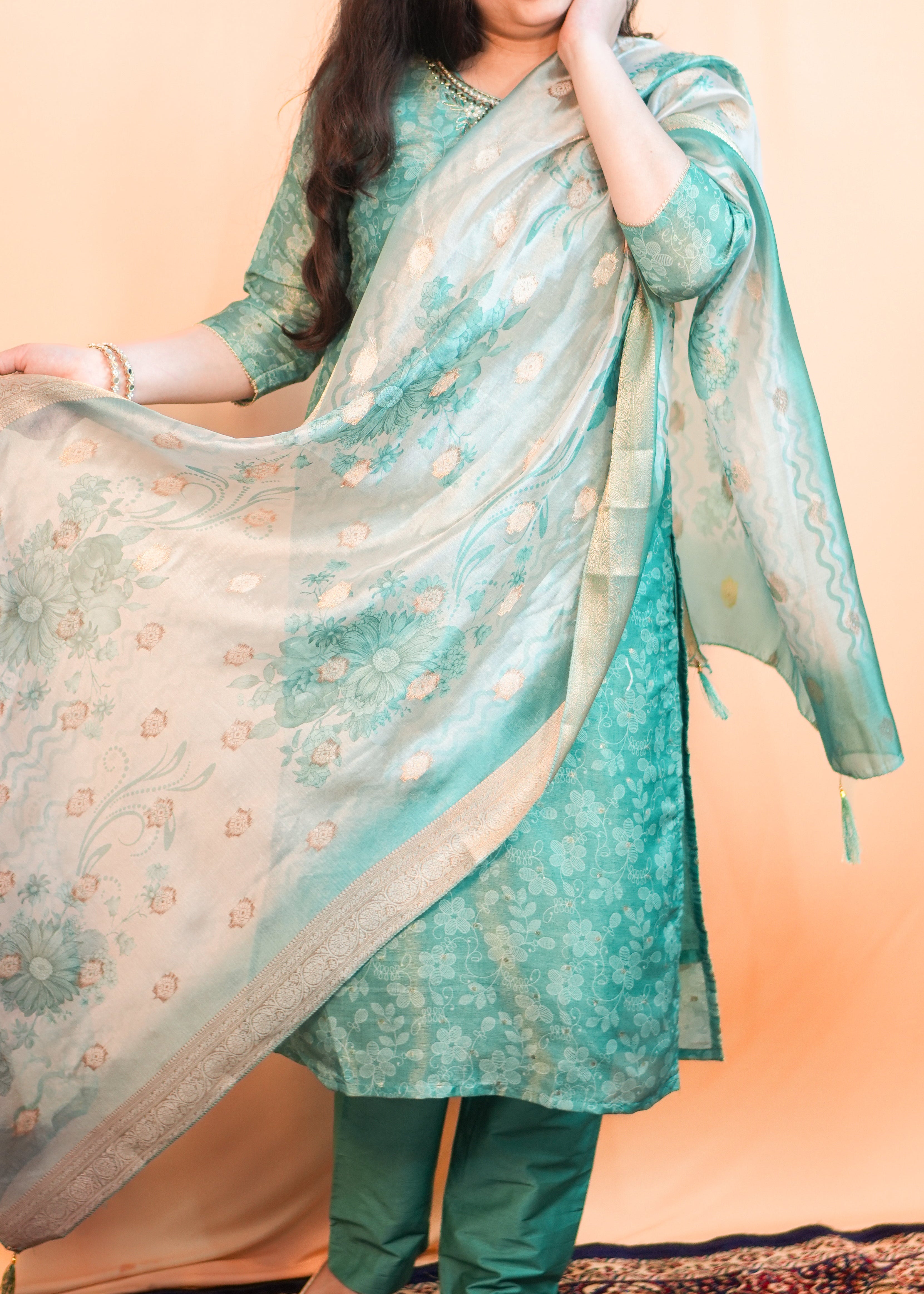 Woman in a green traditional outfit with a floral dupatta against a beige background