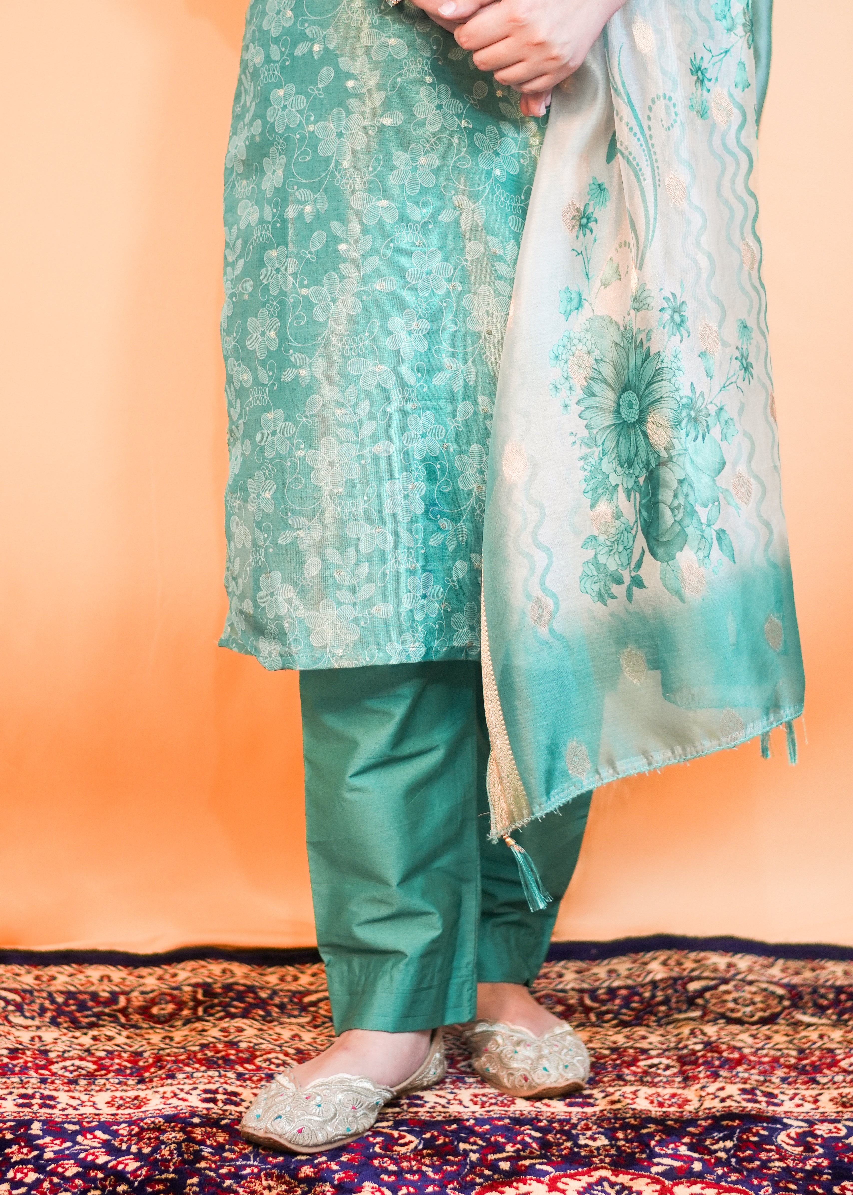 Person wearing a green traditional outfit with a floral dupatta on an orange background
