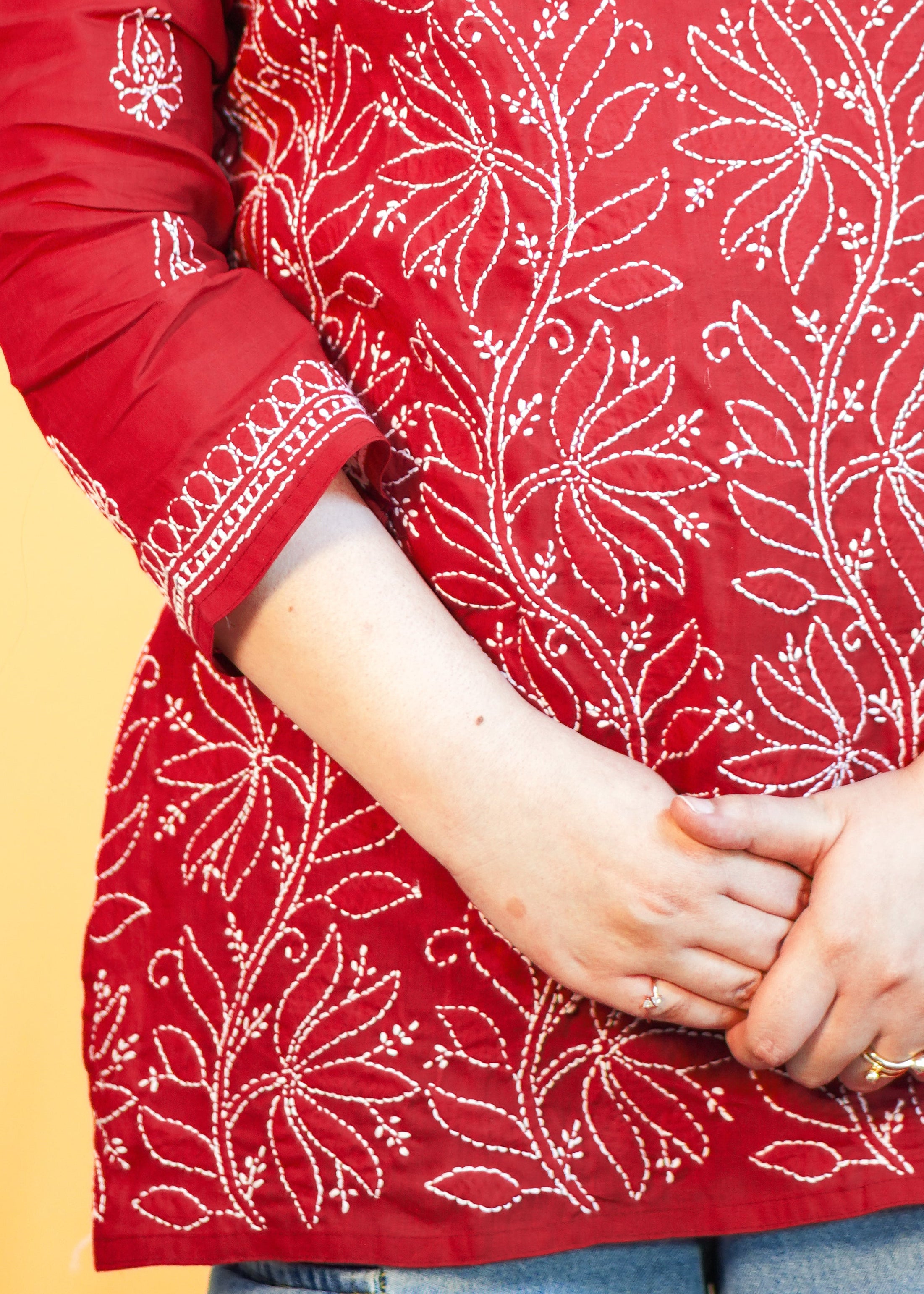Person wearing a red patterned top with blue jeans against a beige background