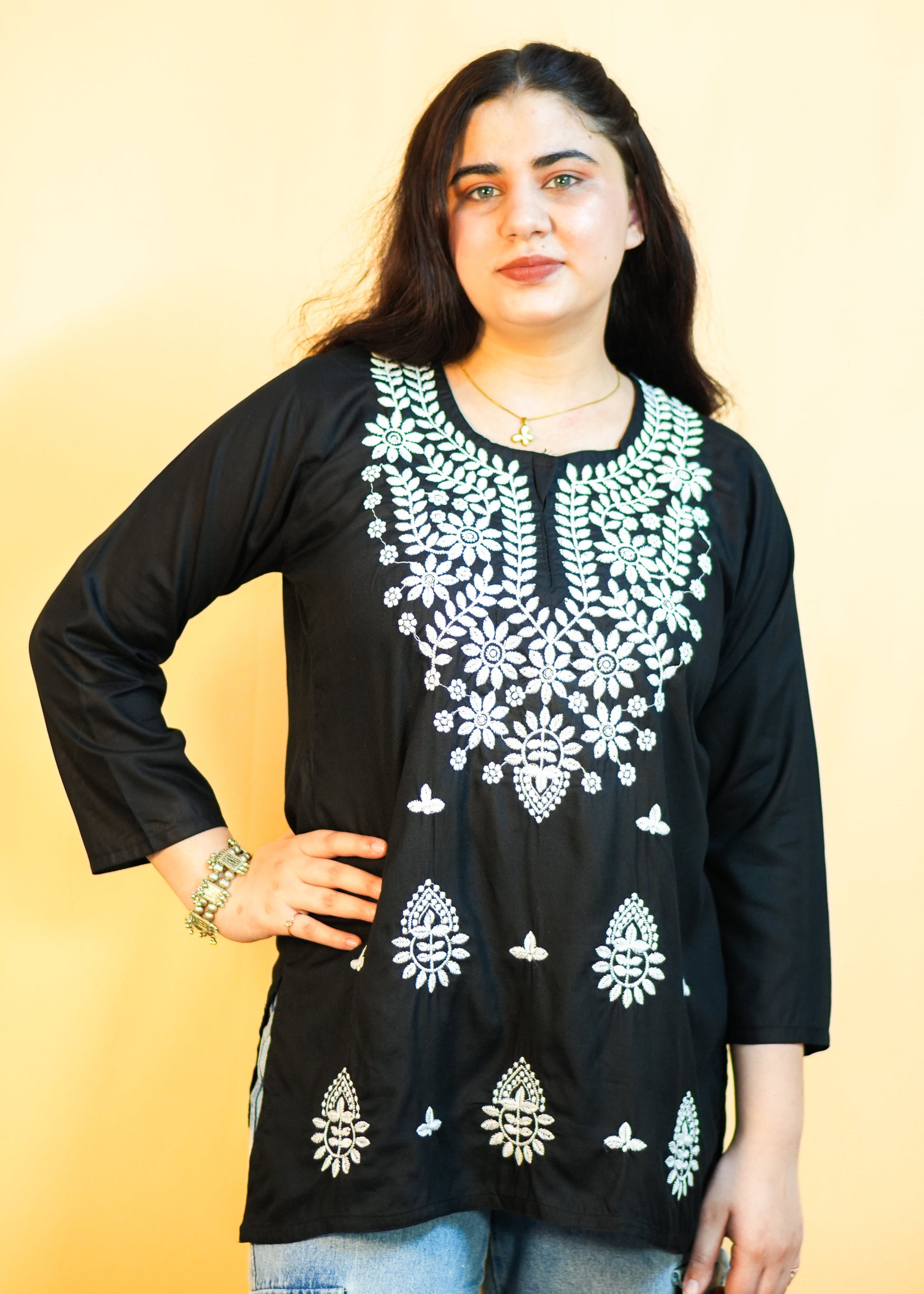 Woman wearing a black embroidered top with white patterns on a yellow background