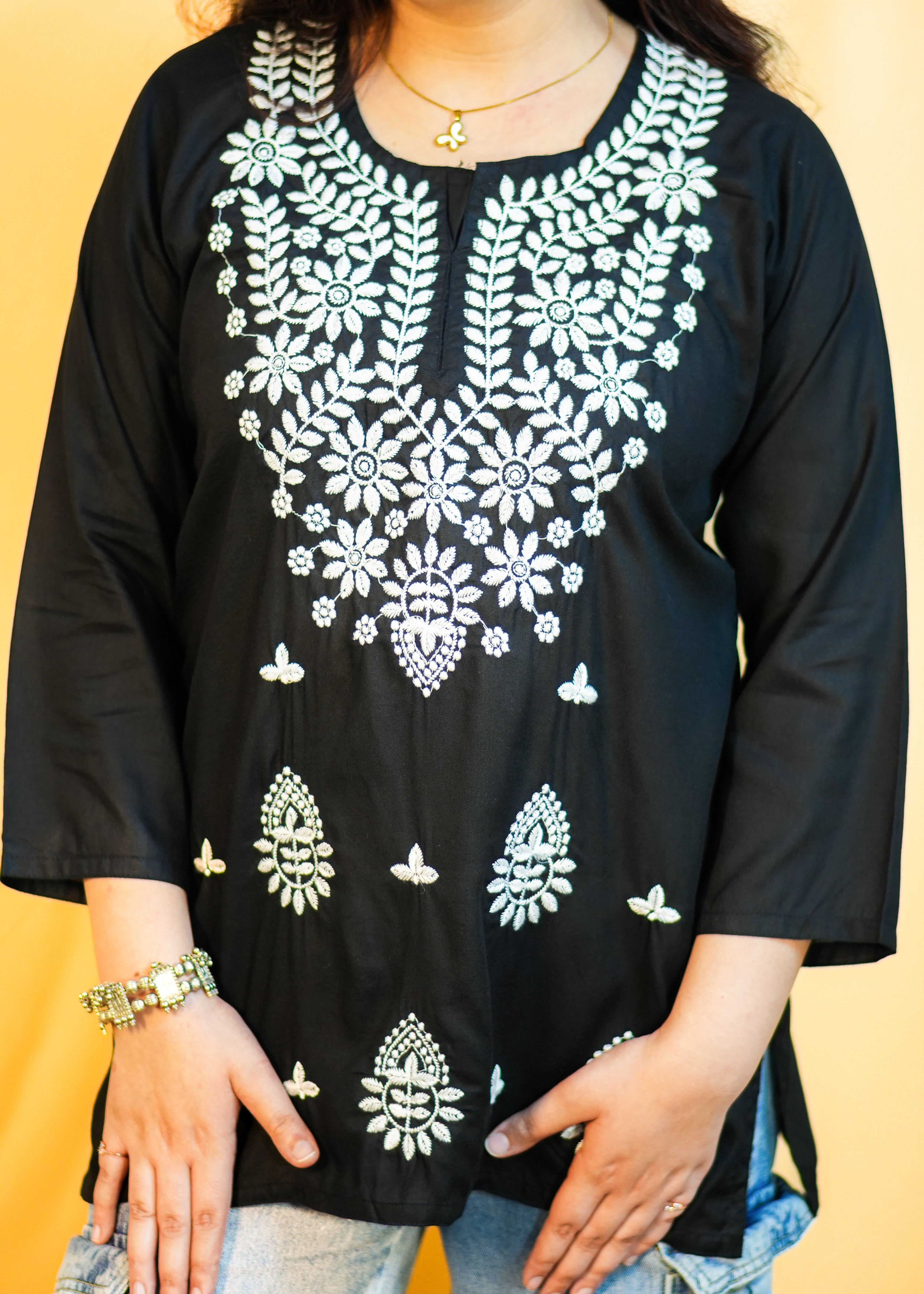 Person wearing a black top with white floral embroidery against a yellow background