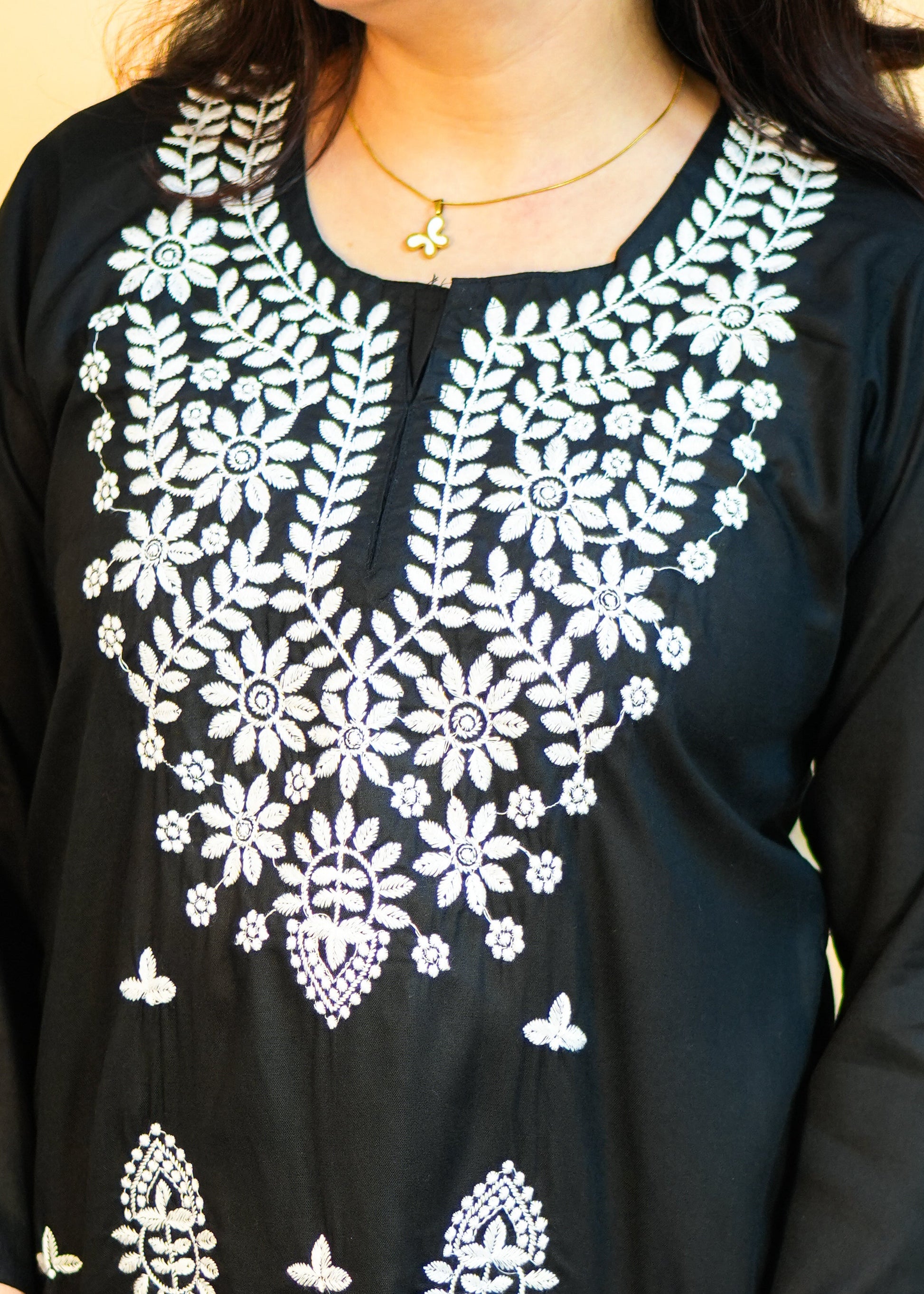 Person wearing a black top with white floral embroidery against a yellow background