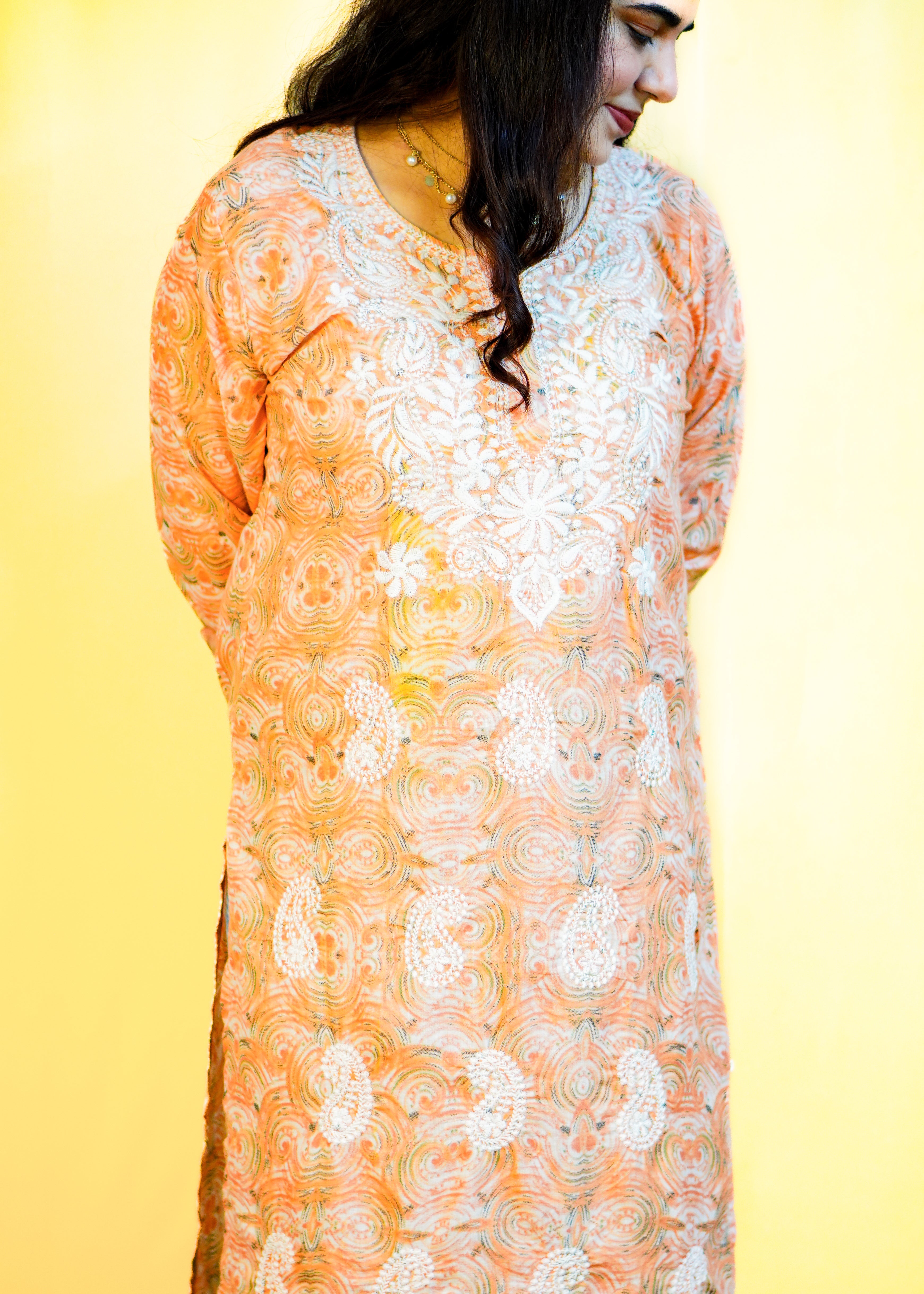 Woman wearing an orange and white floral lace top against a yellow background