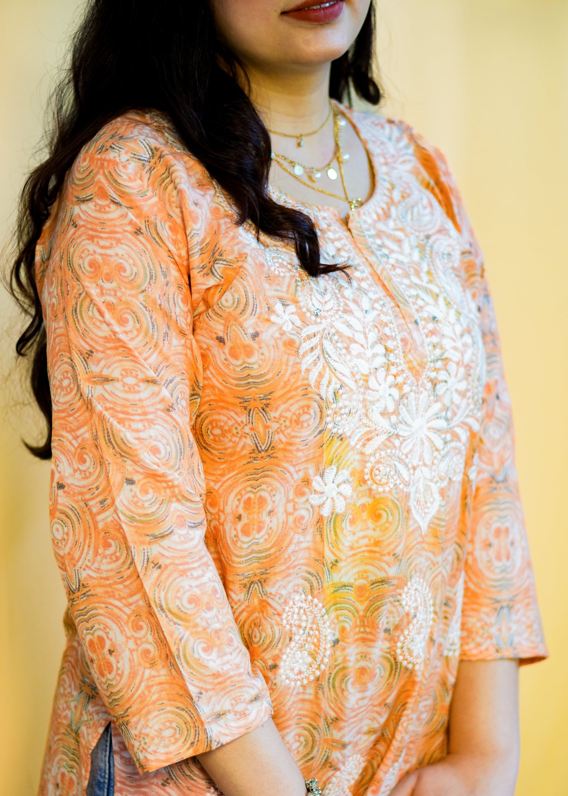 Woman wearing an orange and white patterned kurta against a yellow background