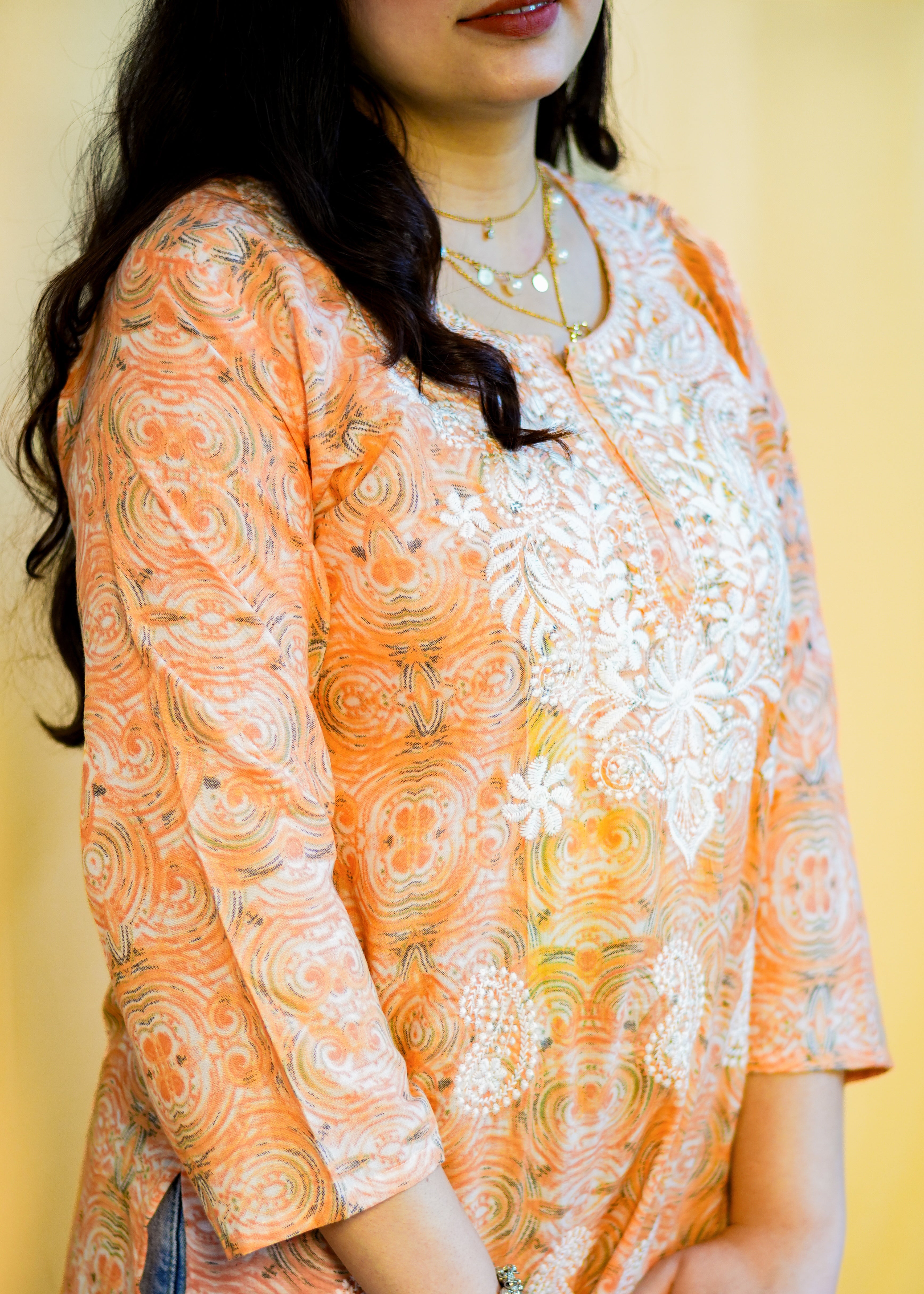 Woman wearing an orange and white patterned kurta against a yellow background