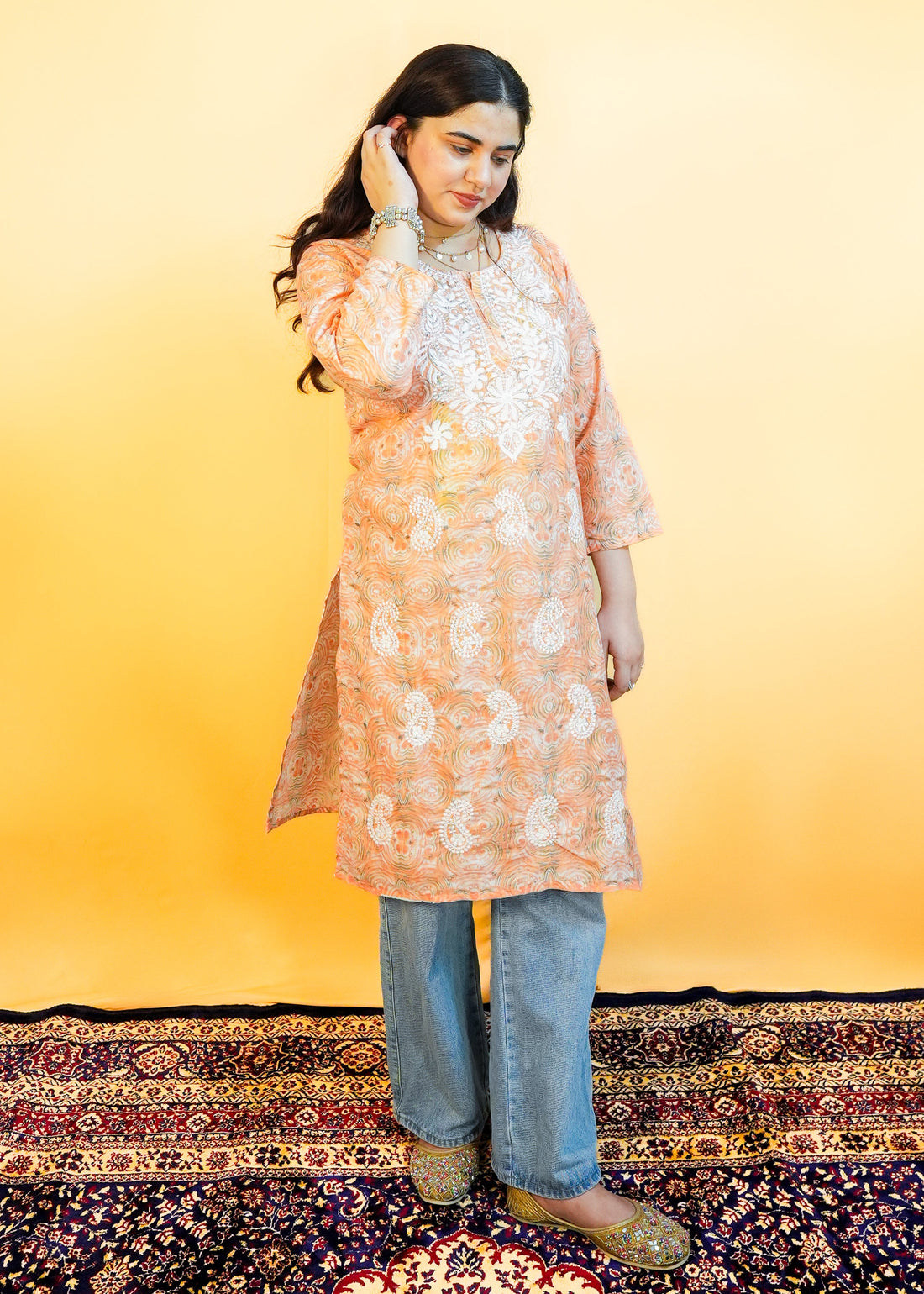 Woman wearing a peach floral kurta with blue jeans on a yellow background
