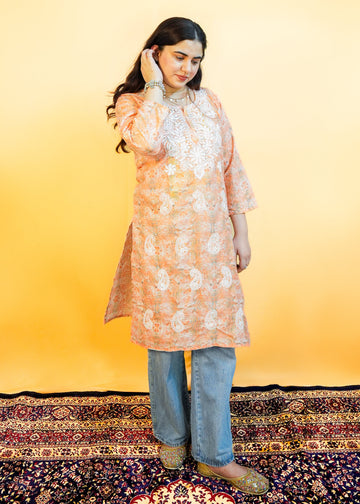 Woman wearing a peach floral kurta with blue jeans on a yellow background