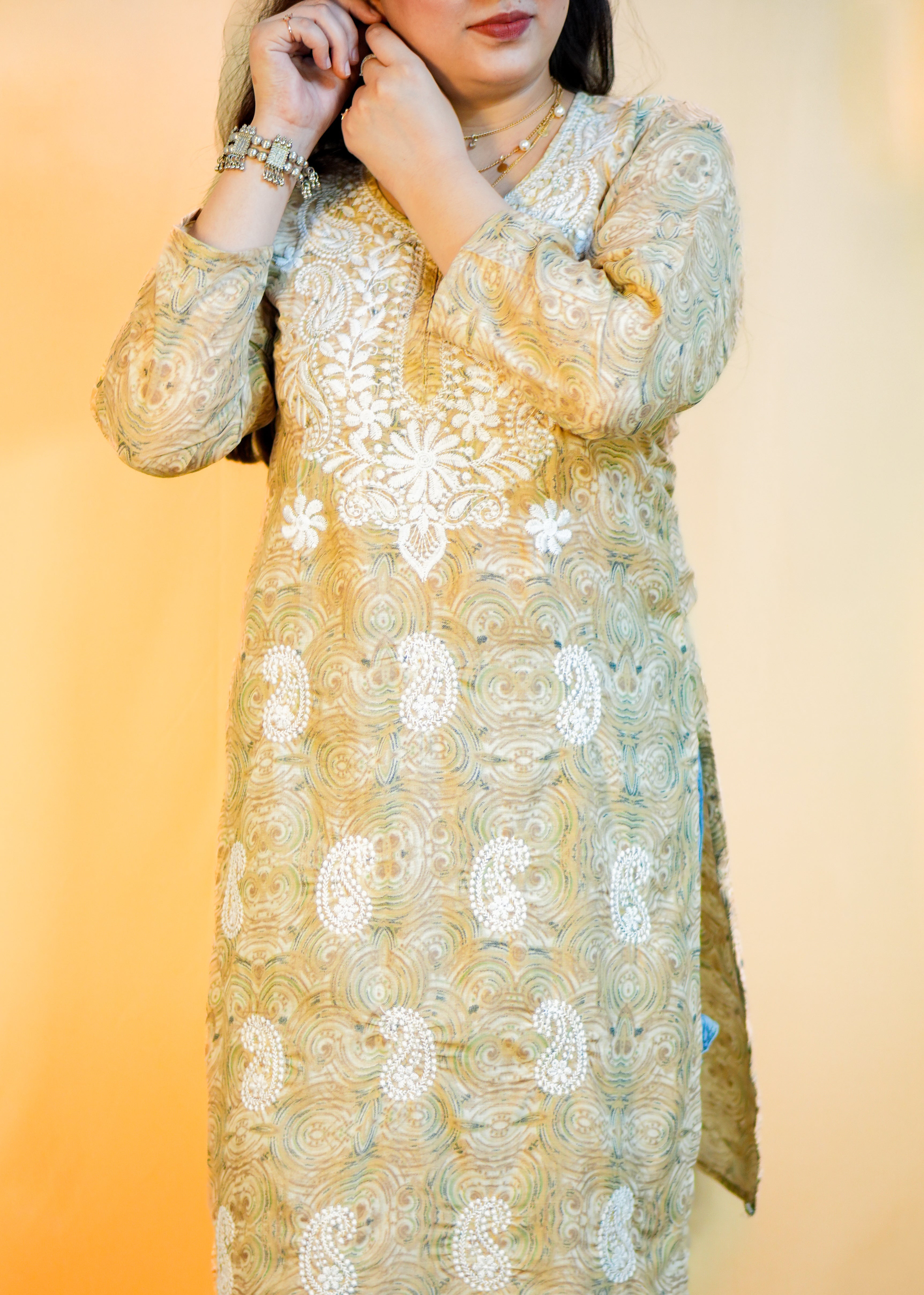 Woman wearing a gold embroidered kurta with blue jeans against an orange gradient background