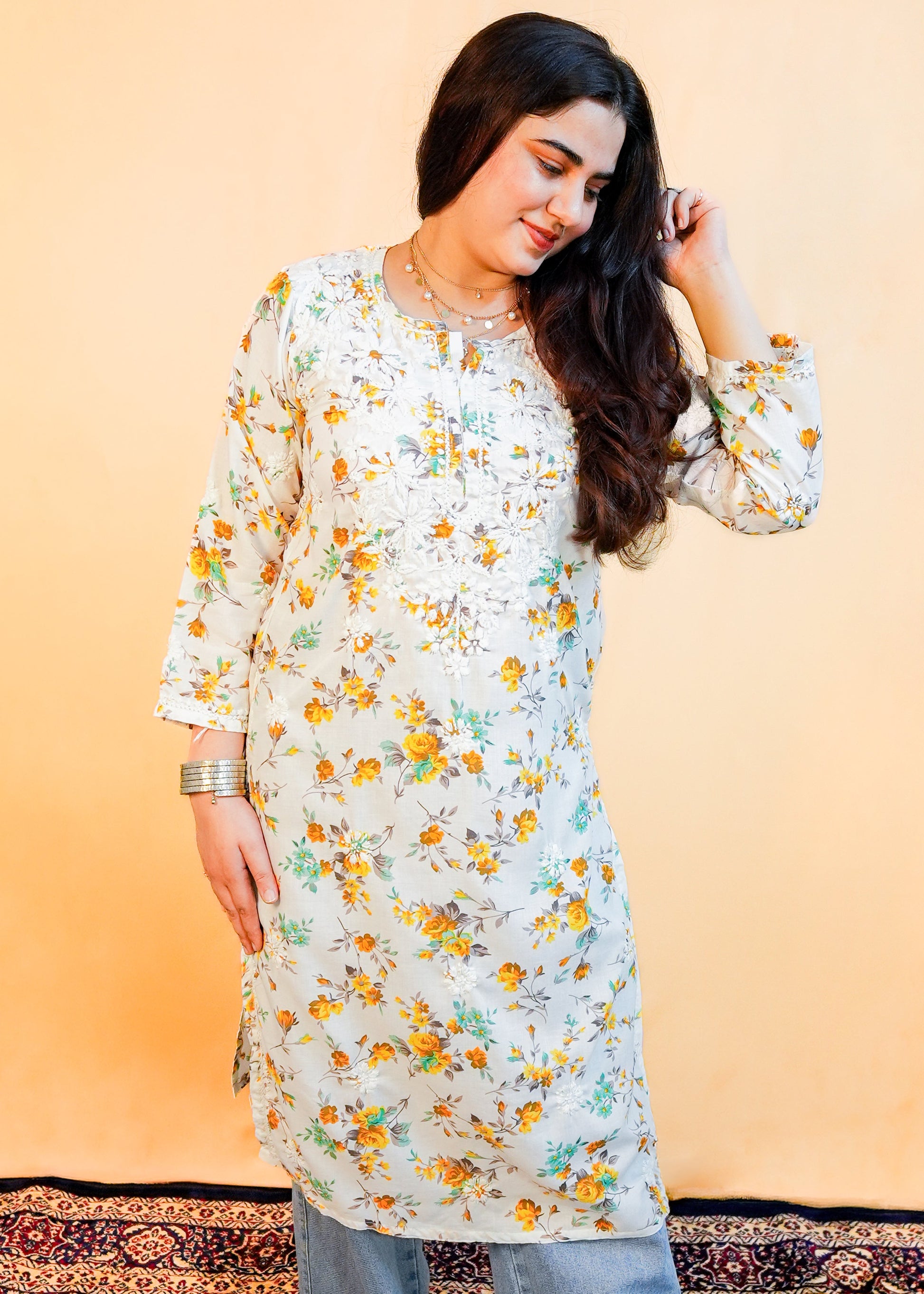 Woman wearing a floral kurta with blue pants on a patterned rug.