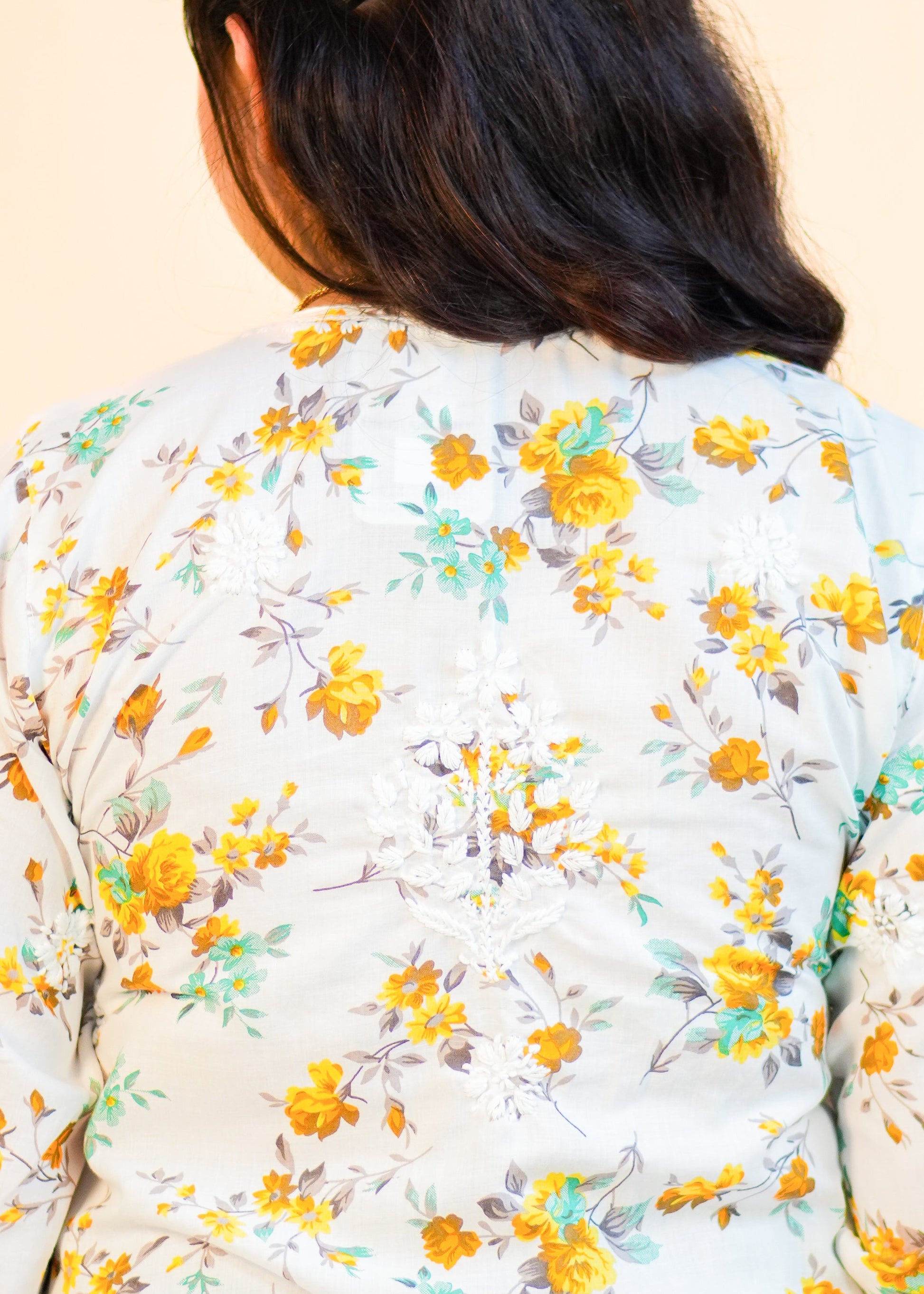 Person wearing a floral dress with yellow flowers on a beige background