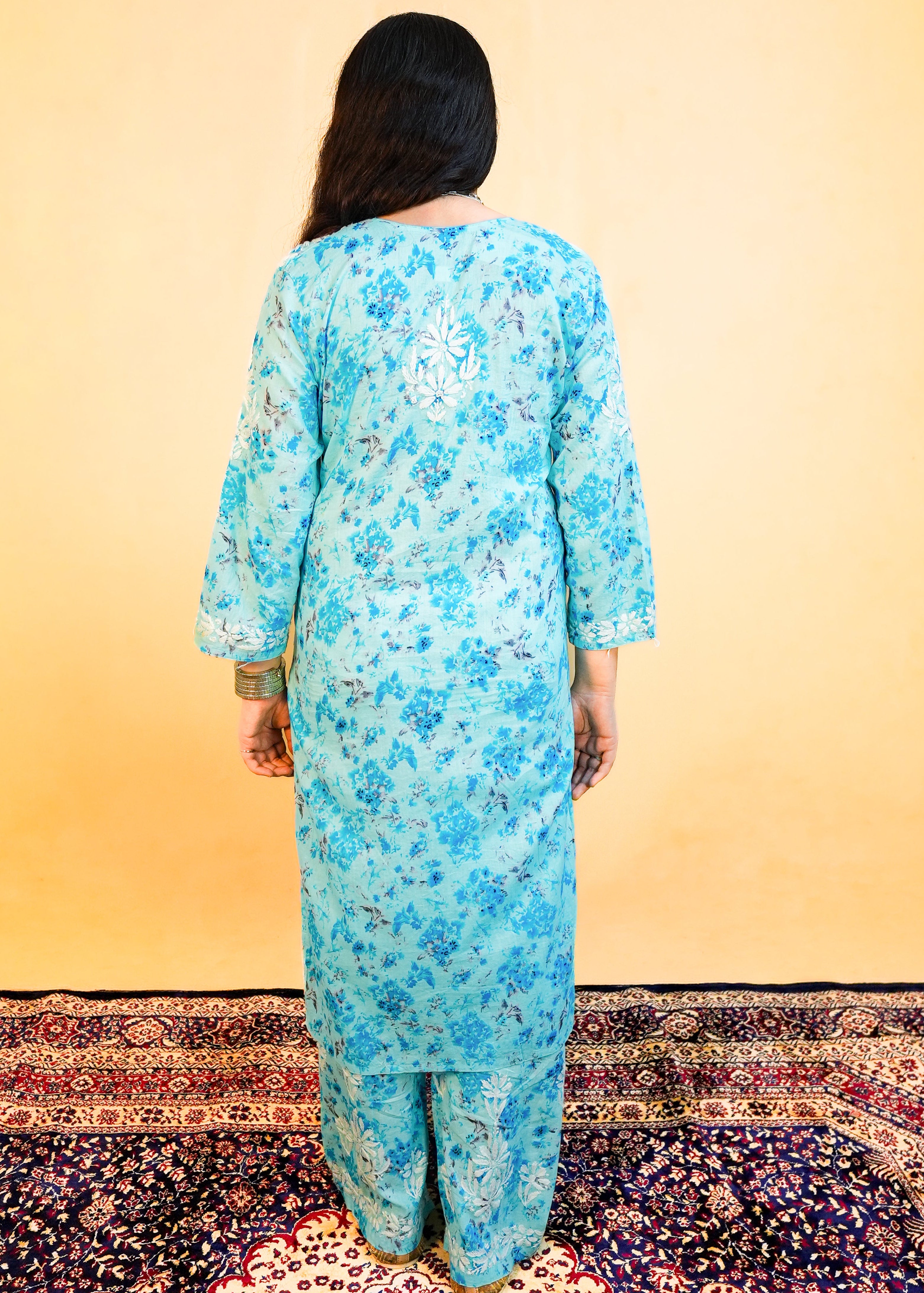 Person wearing a blue floral kurta with pants on a patterned rug.