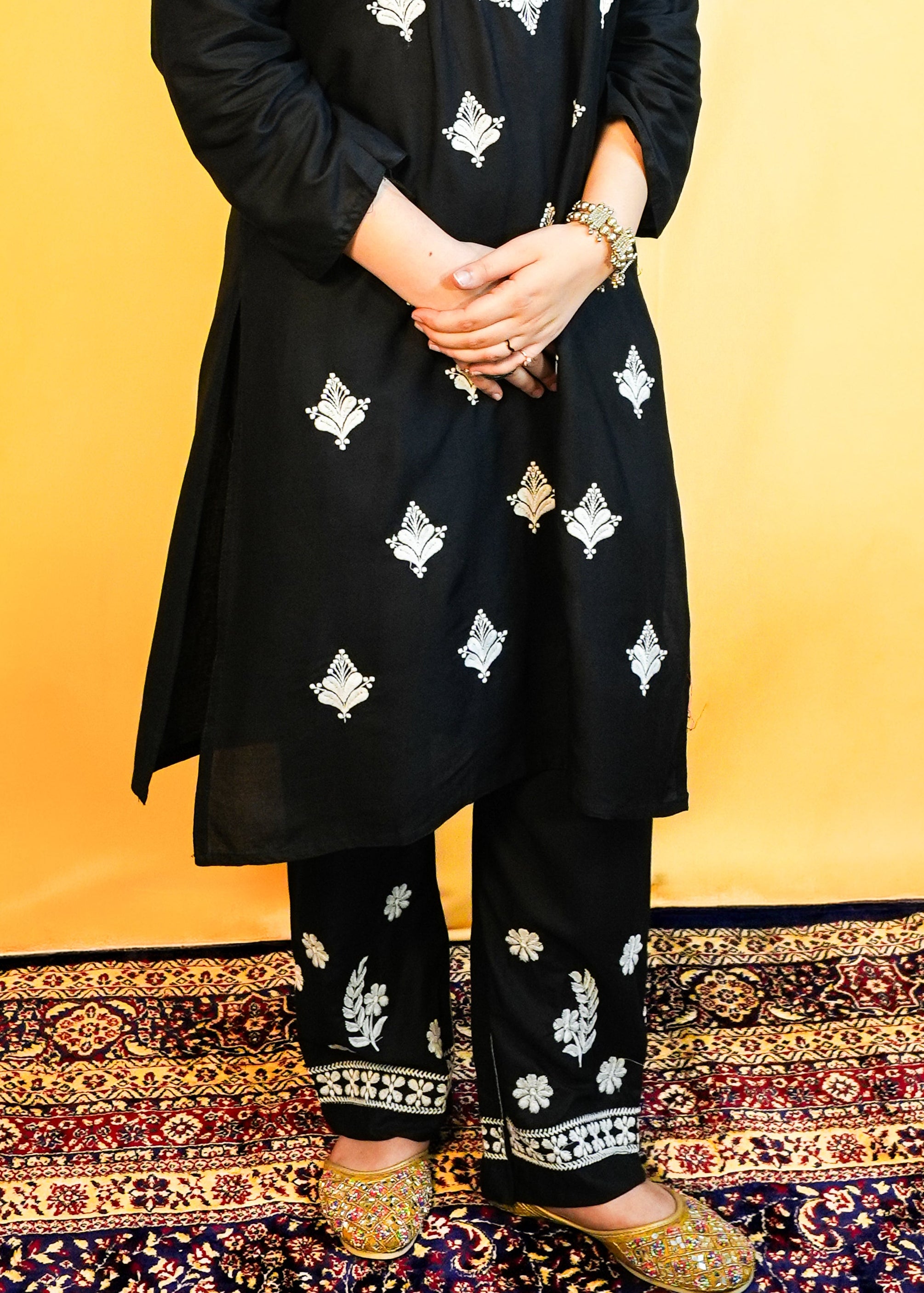 Woman wearing a black traditional outfit with white embroidery against a yellow background