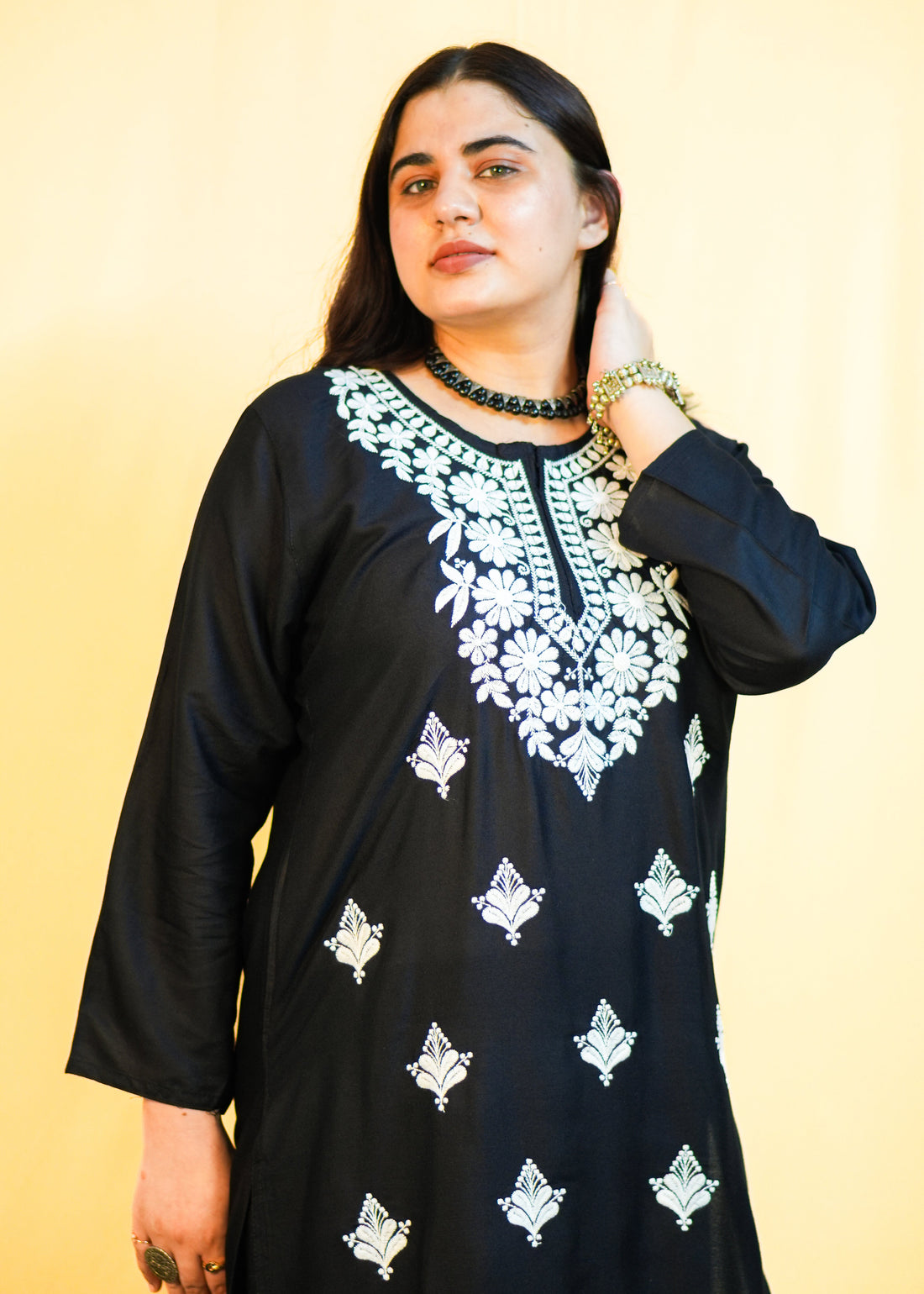 Woman wearing a black dress with white embroidery against a yellow background