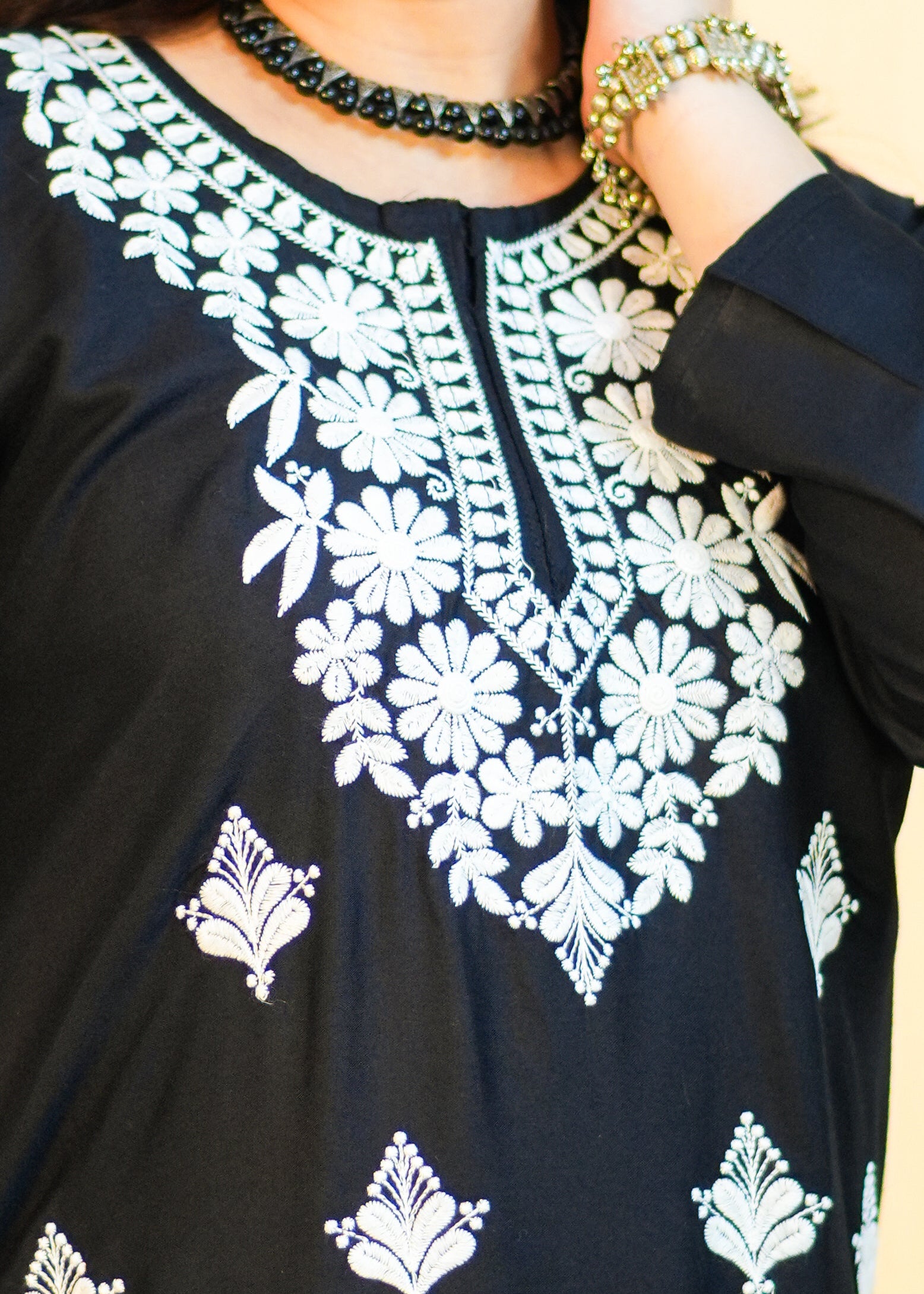 Woman wearing a black dress with white embroidery against a yellow background
