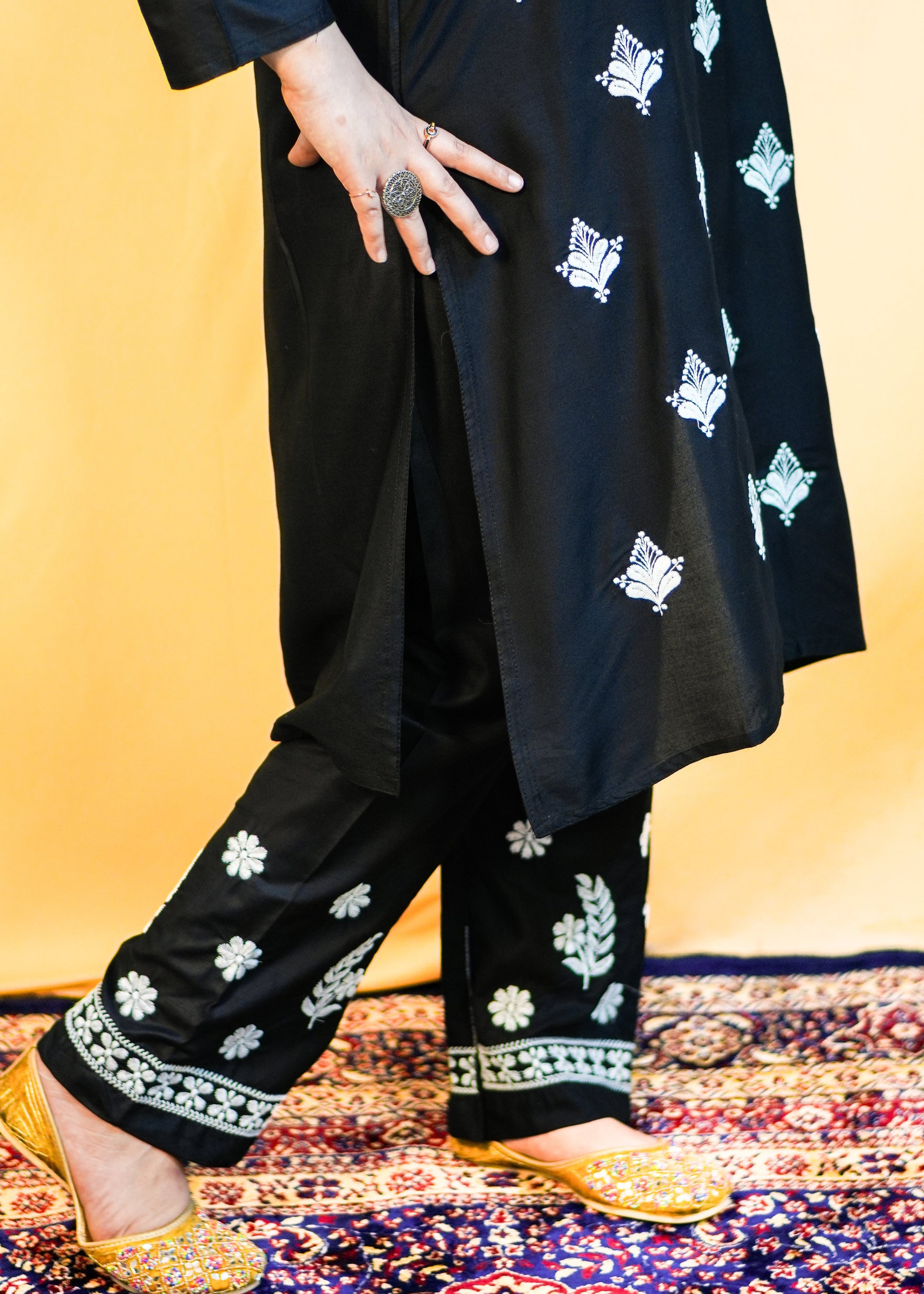 Person wearing a black outfit with white floral patterns on a colorful rug.