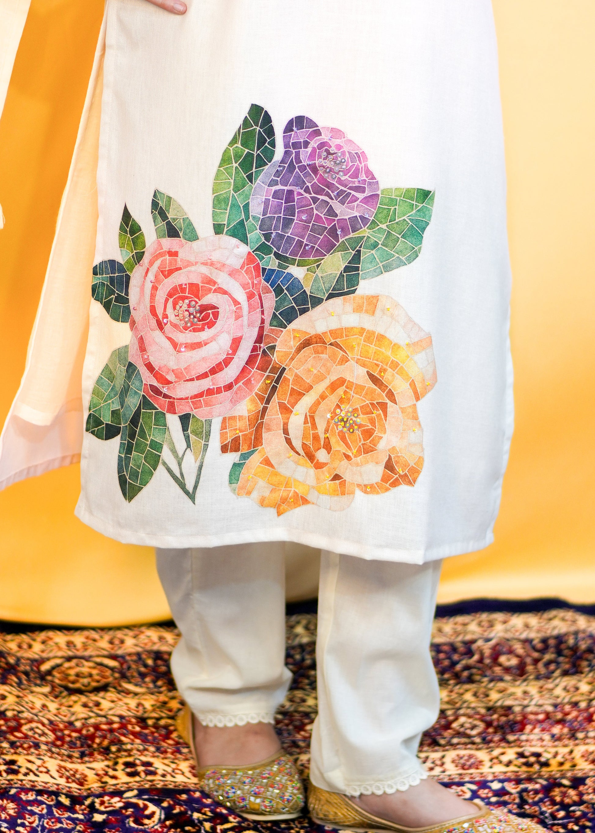 Person wearing a white outfit with colorful floral patterns on a patterned carpet.