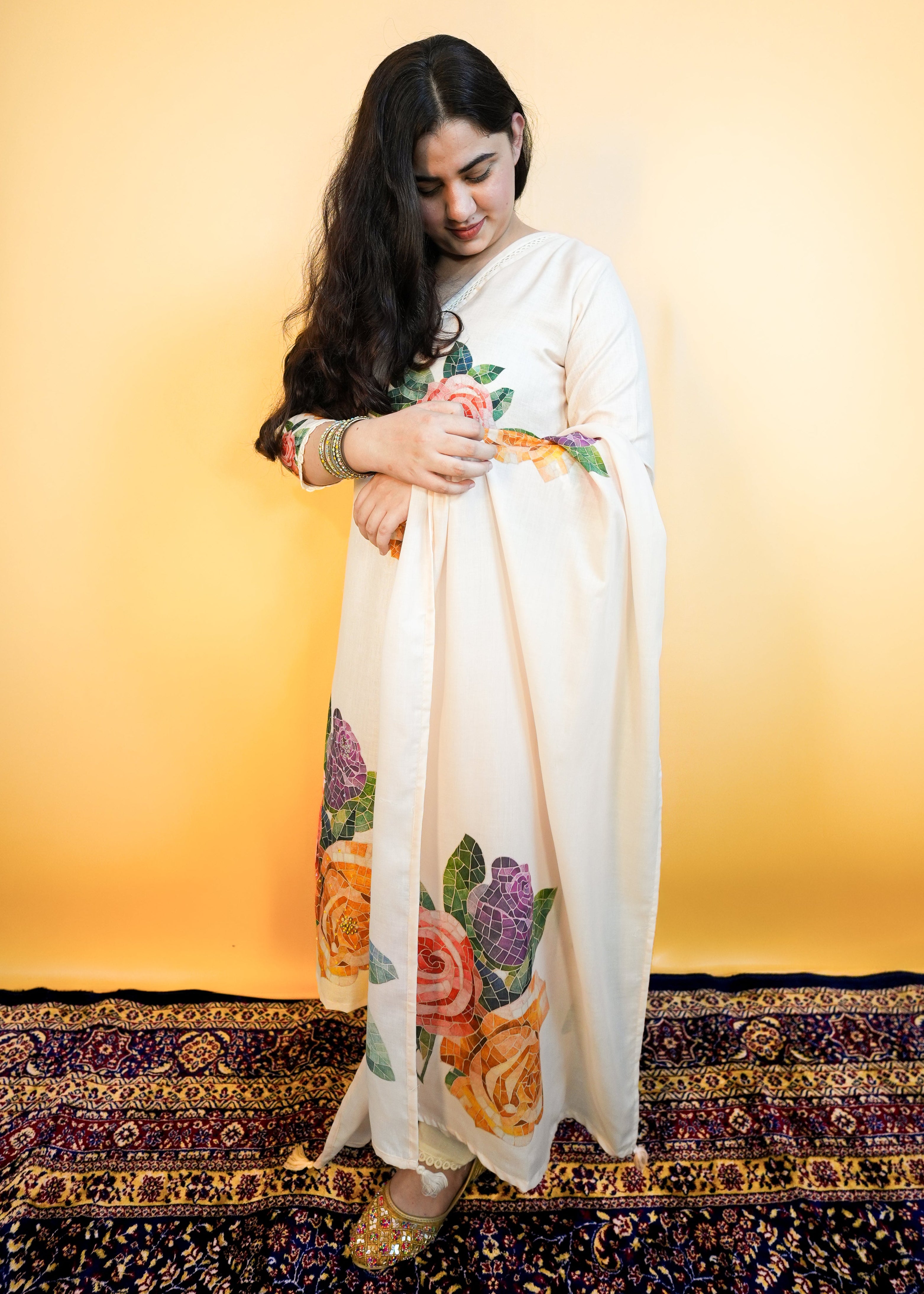 Woman in a floral dress standing on a patterned rug with a yellow wall background