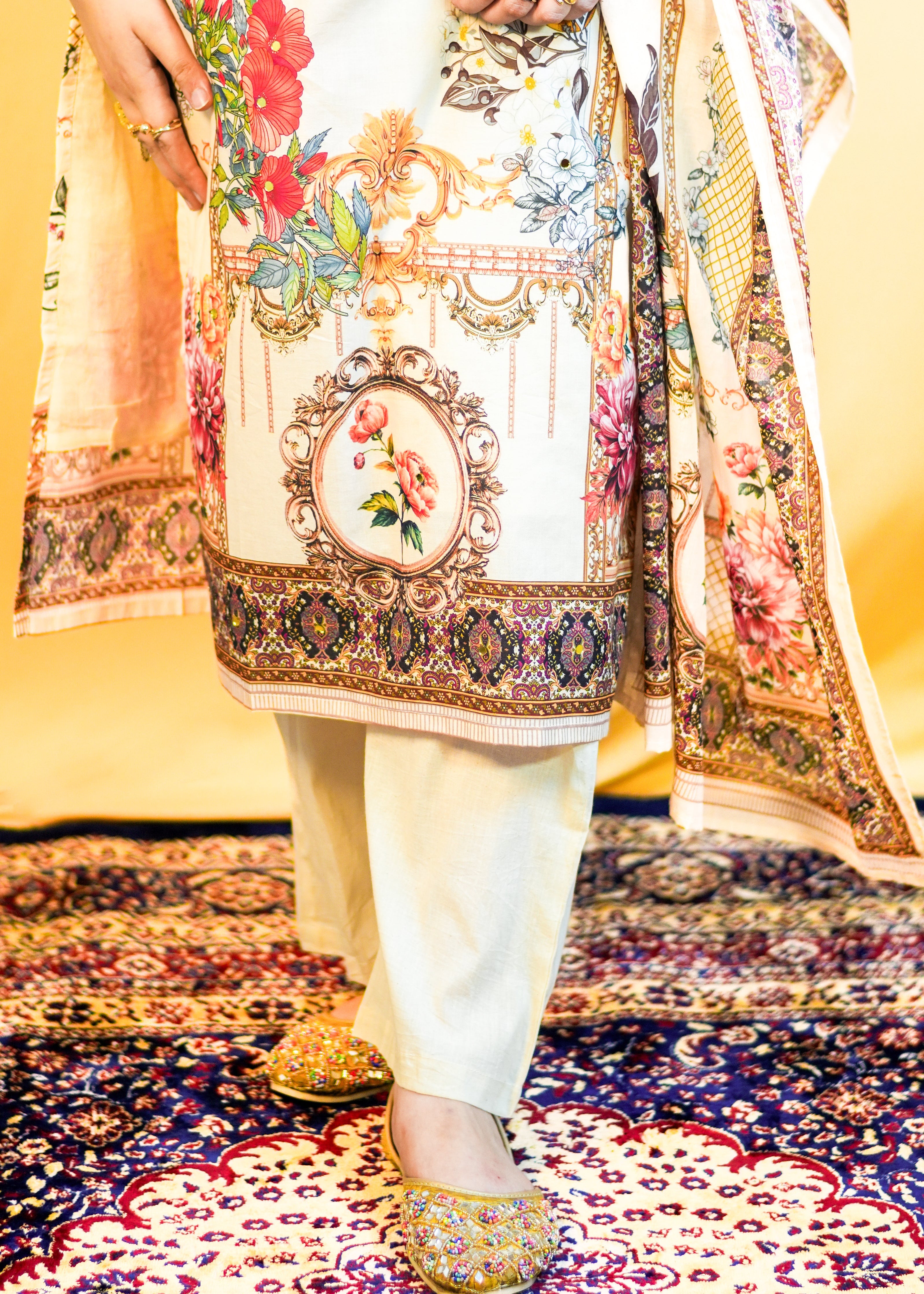 Person wearing a colorful traditional outfit with floral and geometric patterns on a patterned carpet.