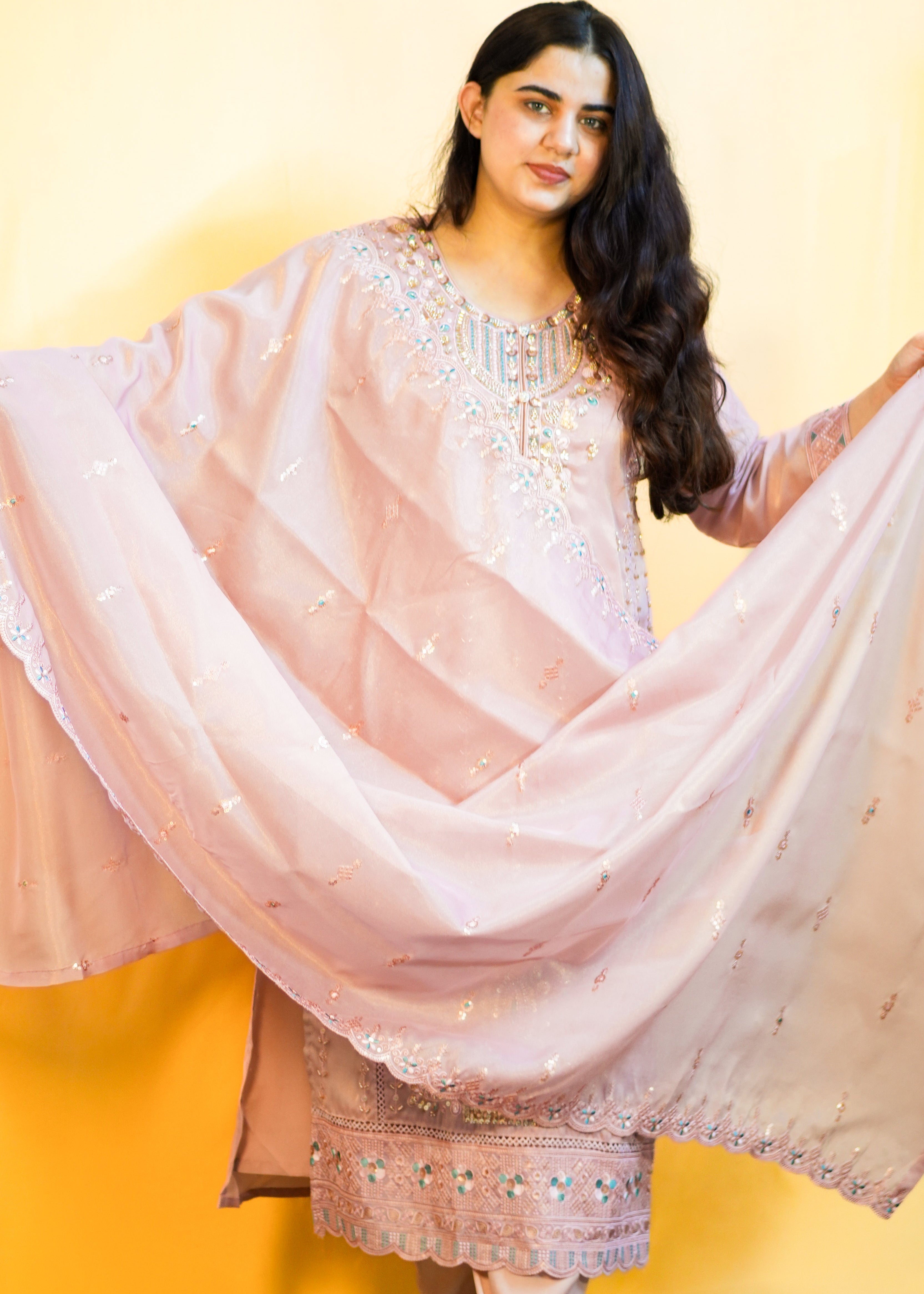 Woman in a traditional outfit with a pink dupatta against a yellow background