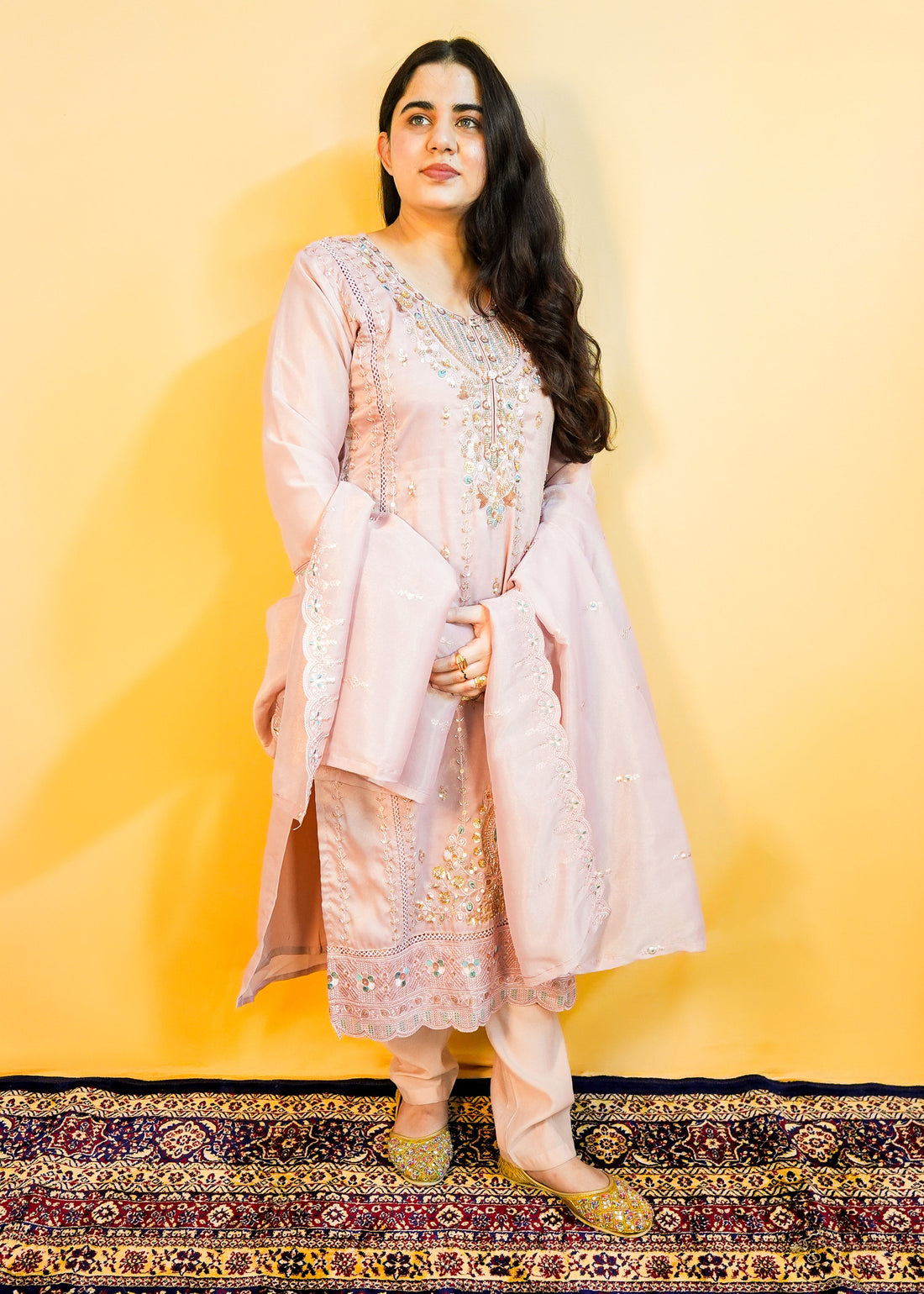 Woman in a traditional outfit with a pink dupatta against a yellow background