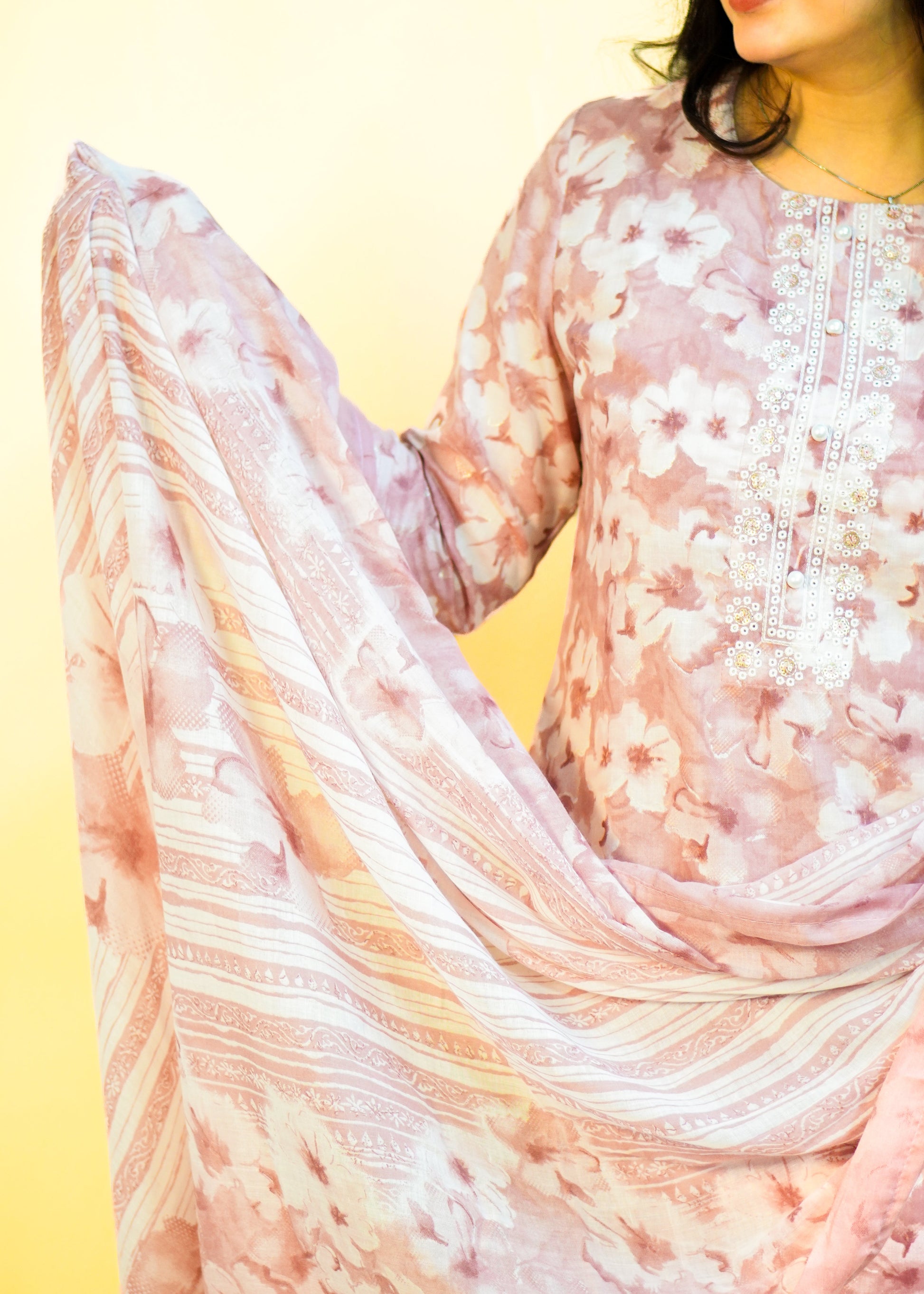 Person wearing a floral dress with a light pink scarf on a yellow background
