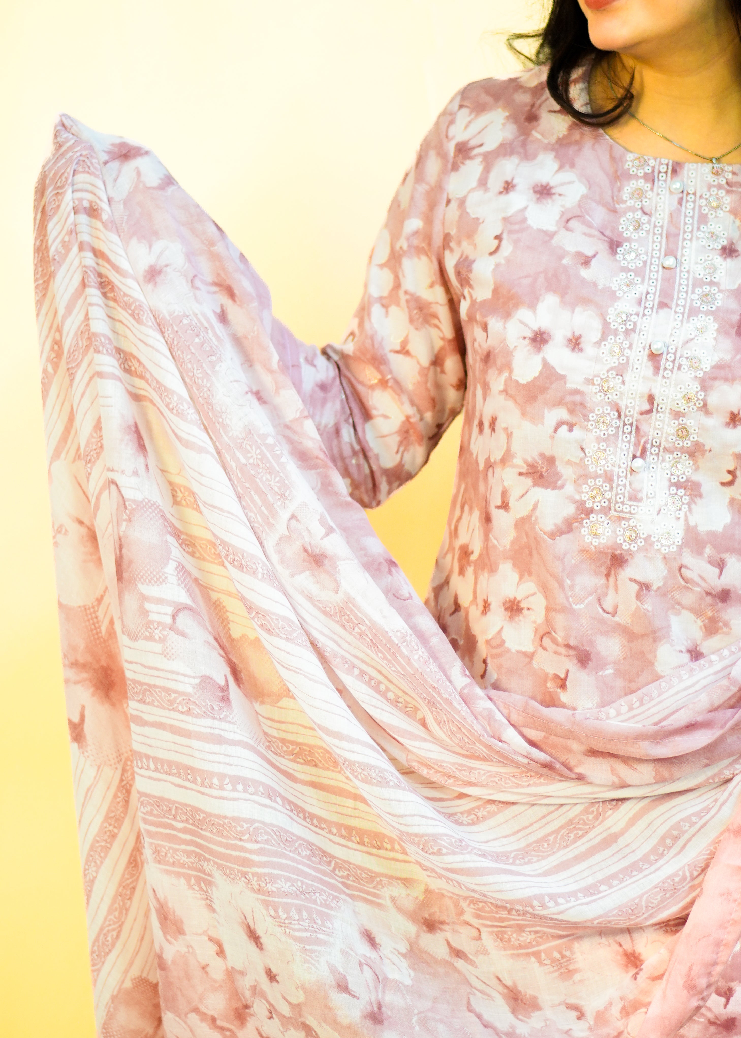 Person wearing a floral dress with a light pink scarf on a yellow background