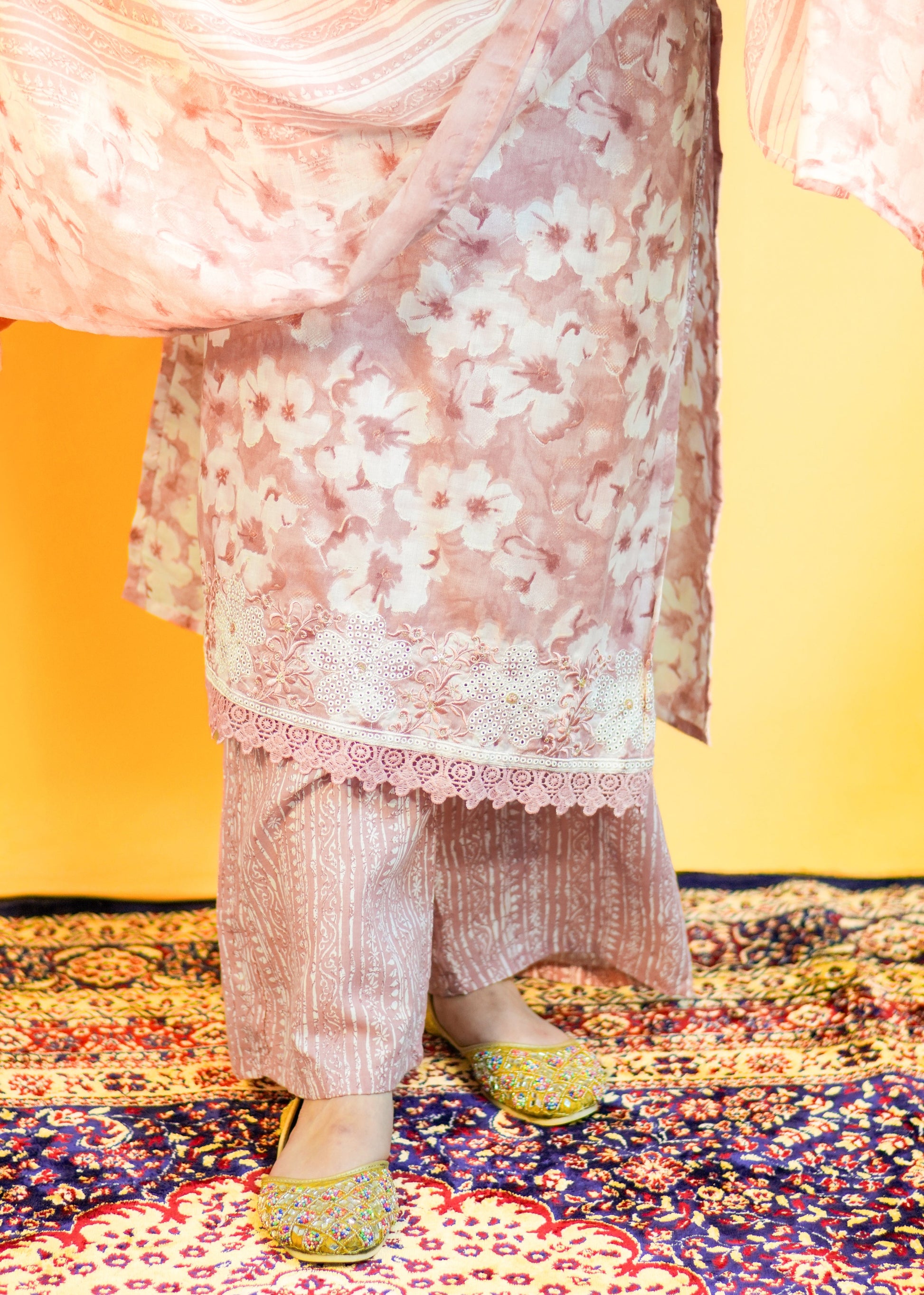 Person wearing a floral dress and colorful shoes on a patterned rug