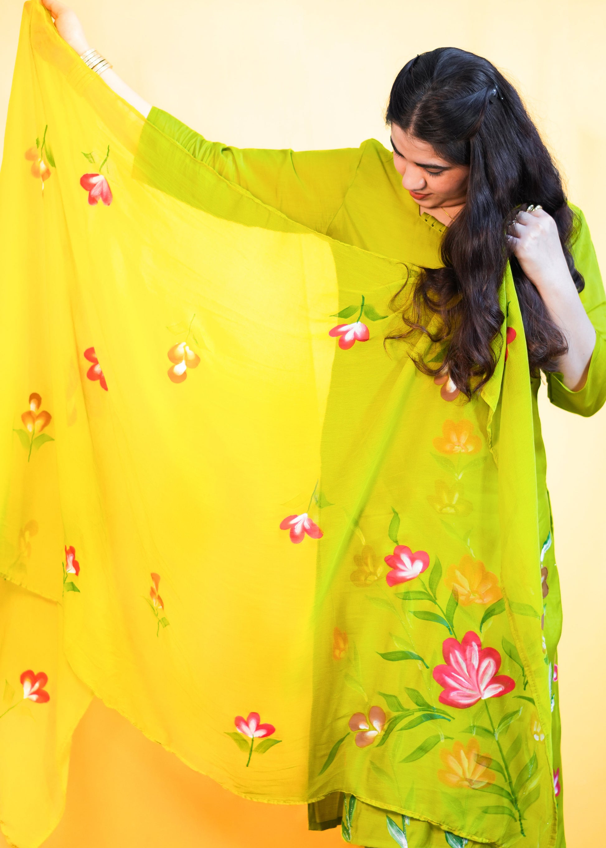 Woman wearing a green embroidered outfit with a yellow dupatta against a yellow background