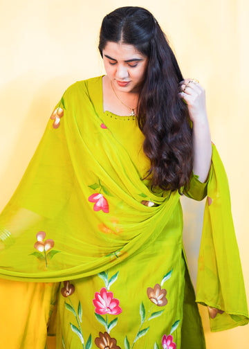 Woman wearing a green saree with floral patterns against a yellow background