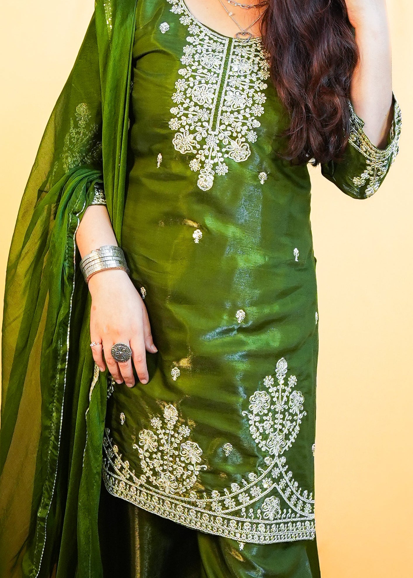 Woman in a green traditional outfit standing on a patterned rug with a yellow wall background