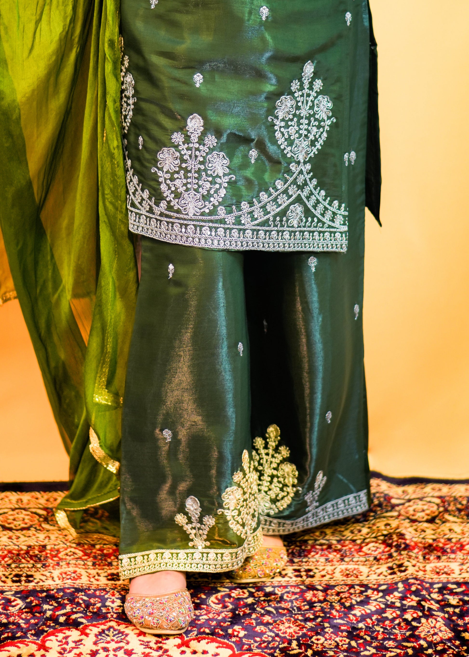 Green traditional outfit with white embroidery on a patterned rug