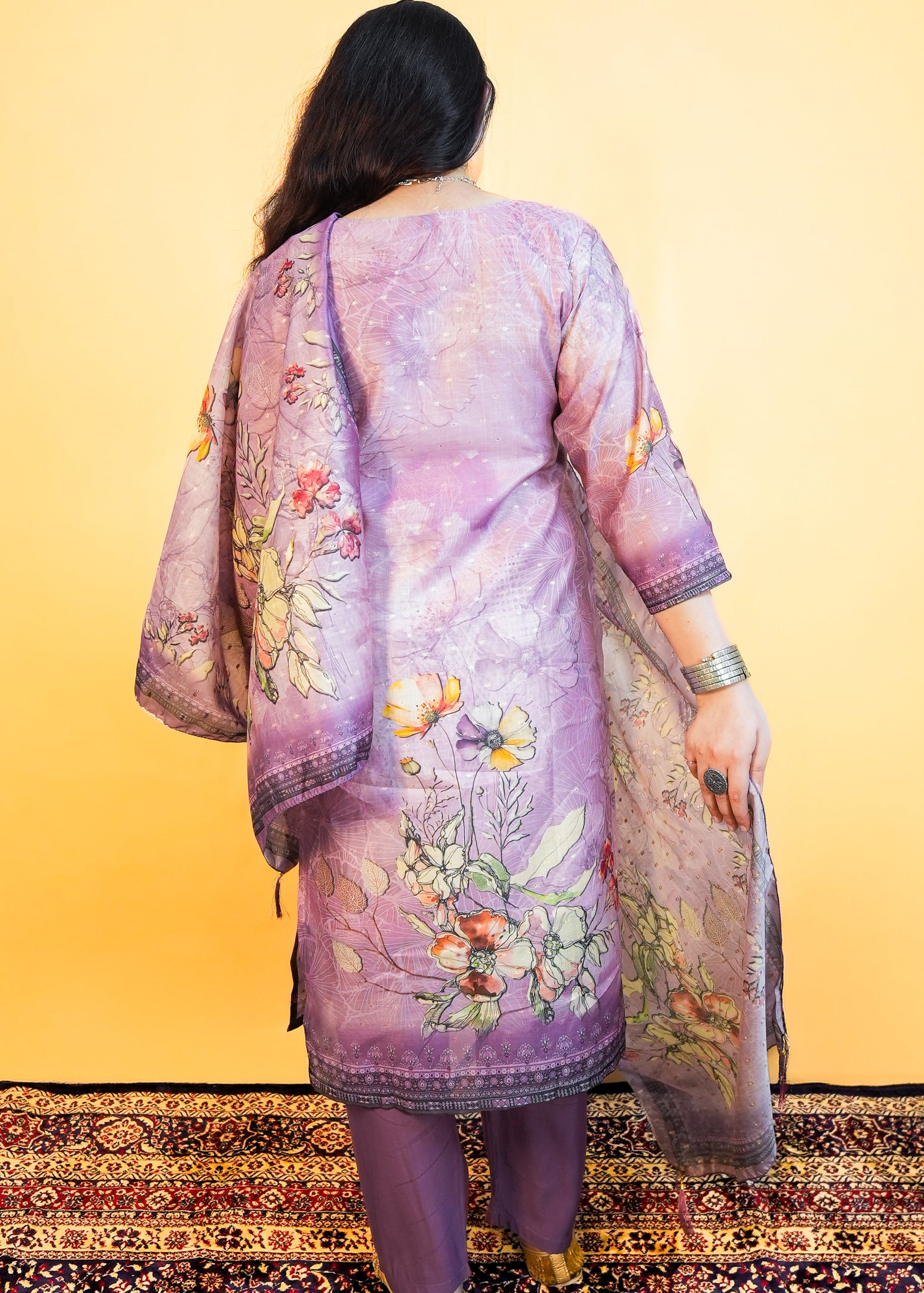 Woman wearing a traditional outfit with a floral design on a patterned rug.