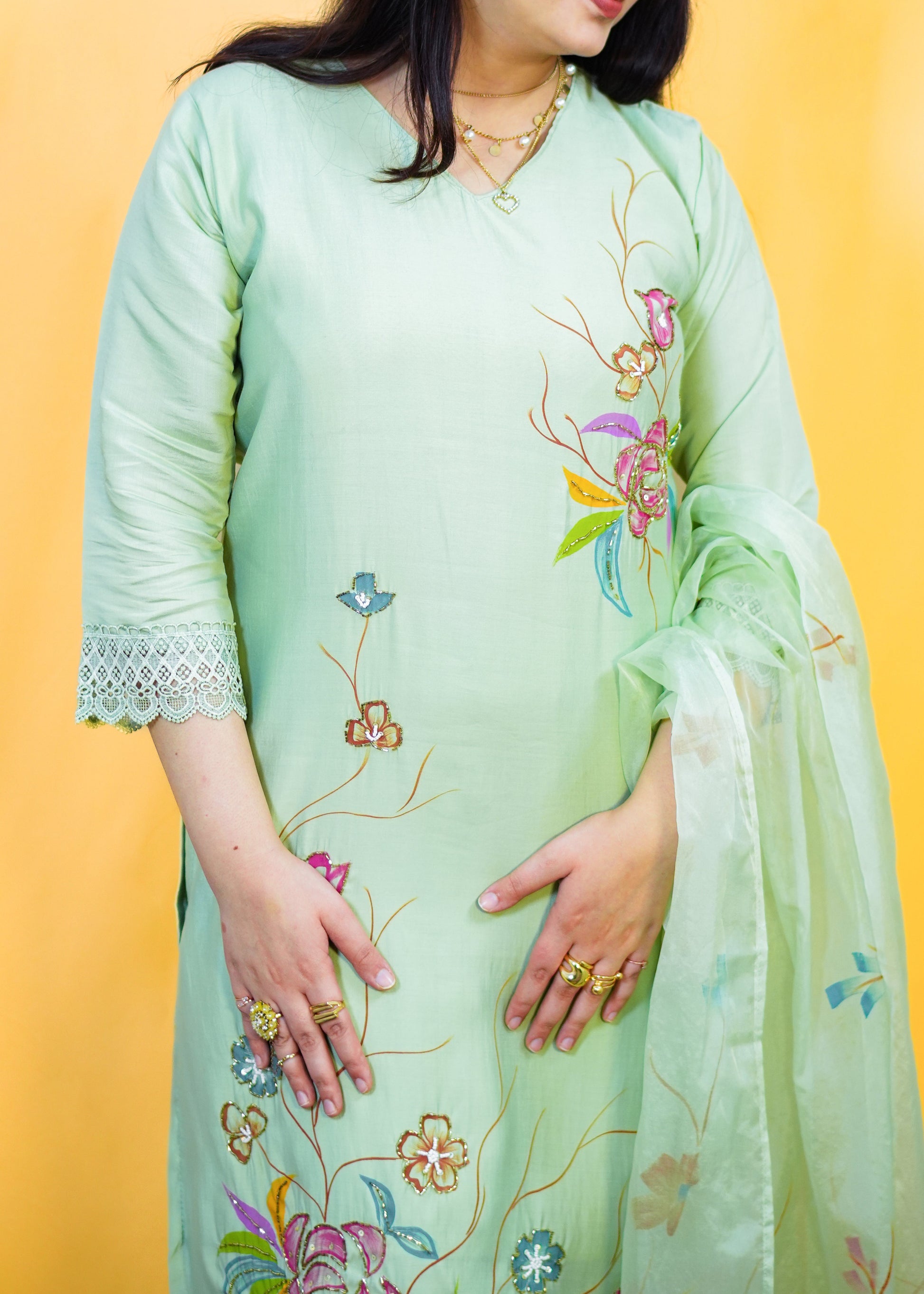 Woman wearing a light green embroidered outfit against a yellow background