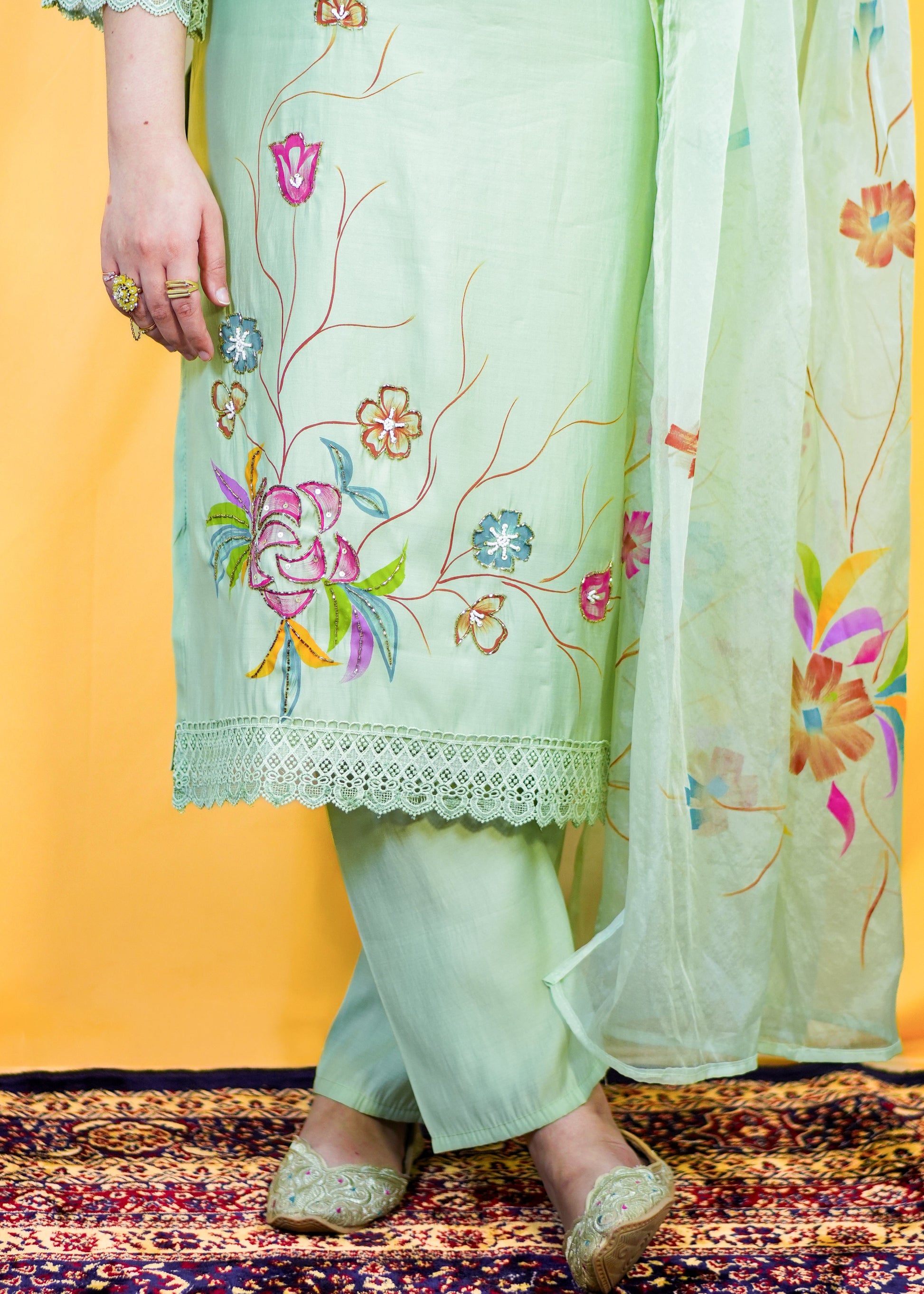 Light green embroidered outfit with a sheer dupatta on a patterned rug.