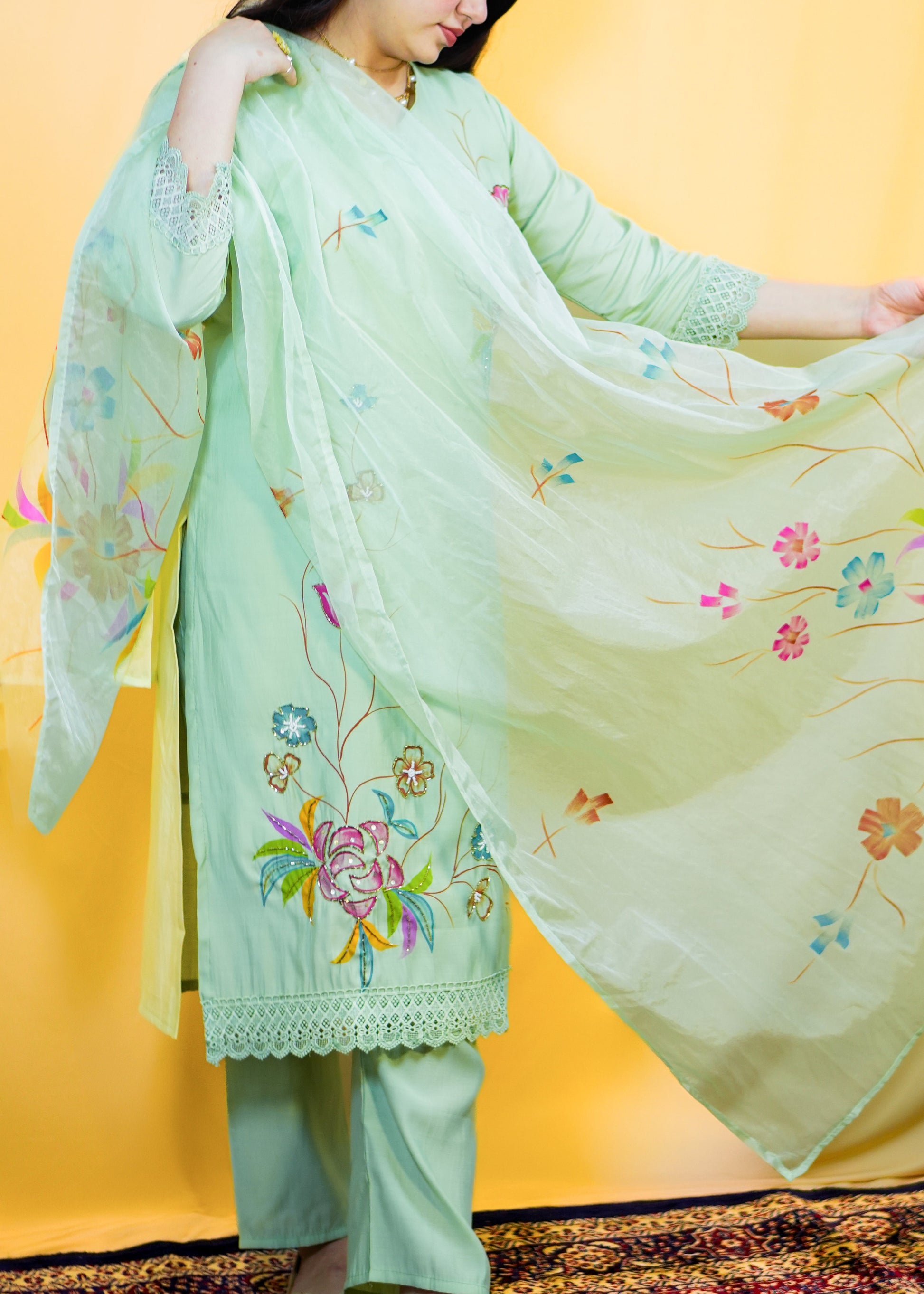 Woman wearing a light green embroidered outfit with a sheer dupatta against a yellow background