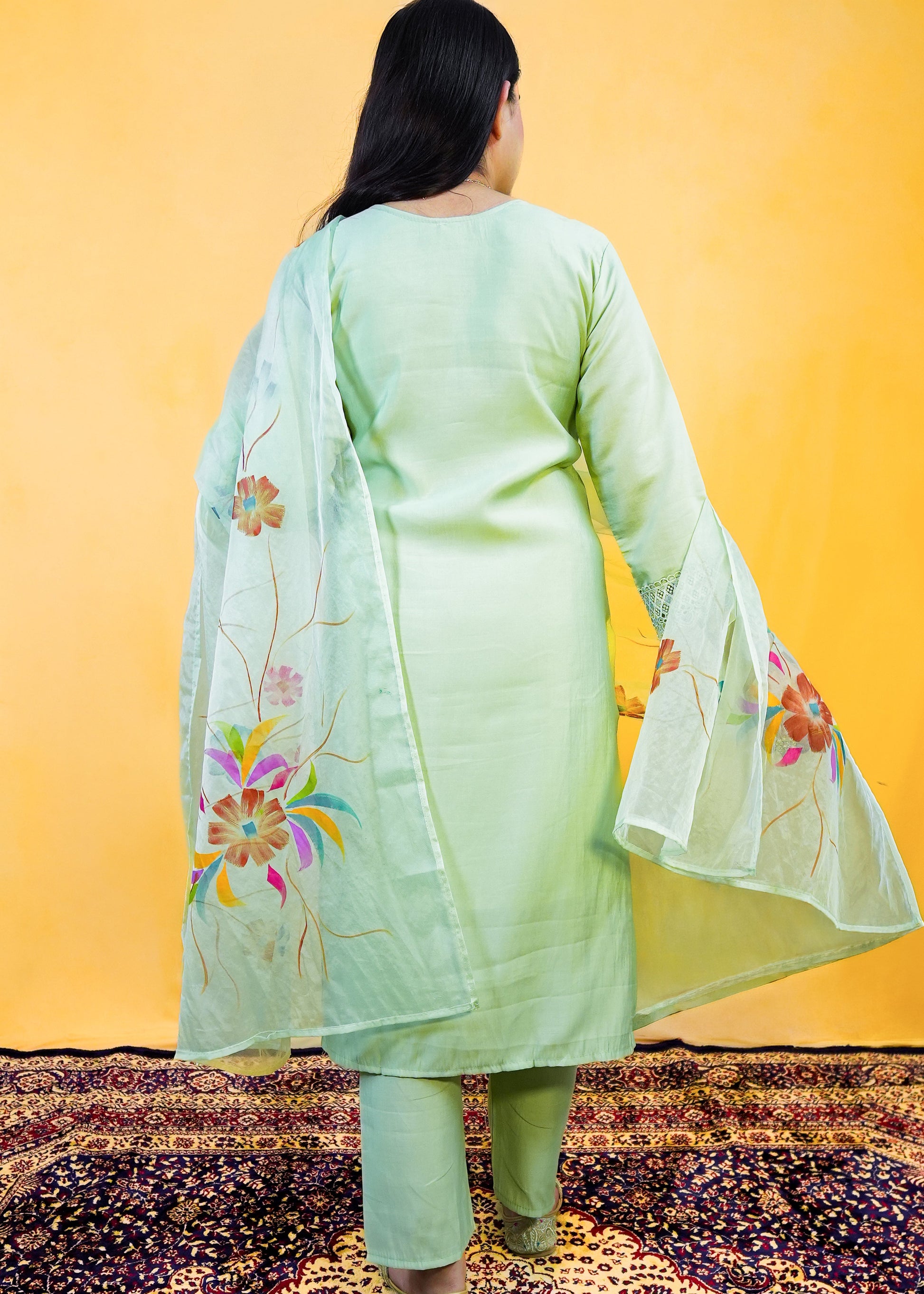 Person wearing a light green traditional outfit with floral patterns on a yellow background