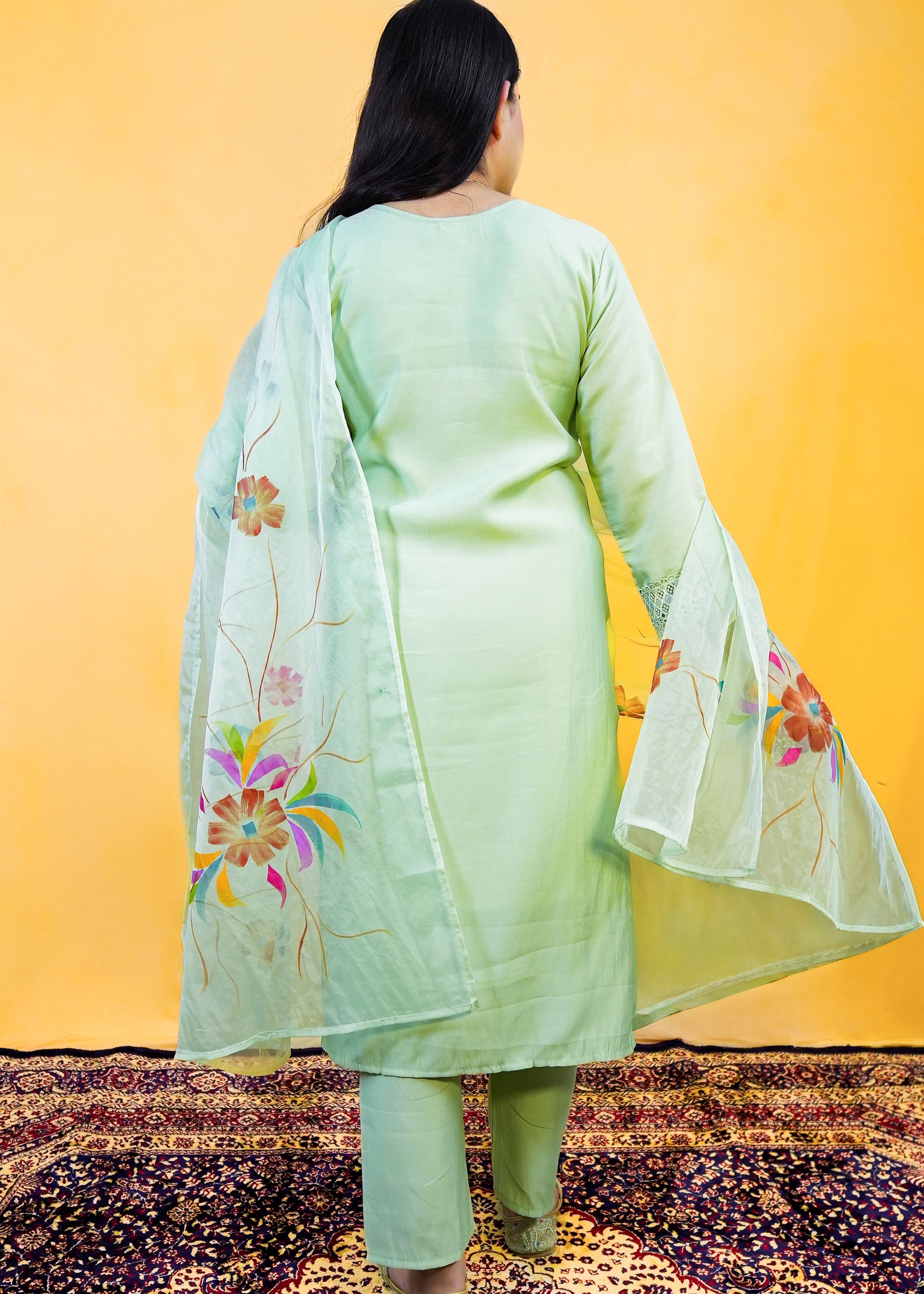 Person wearing a light green traditional outfit with floral patterns on a yellow background