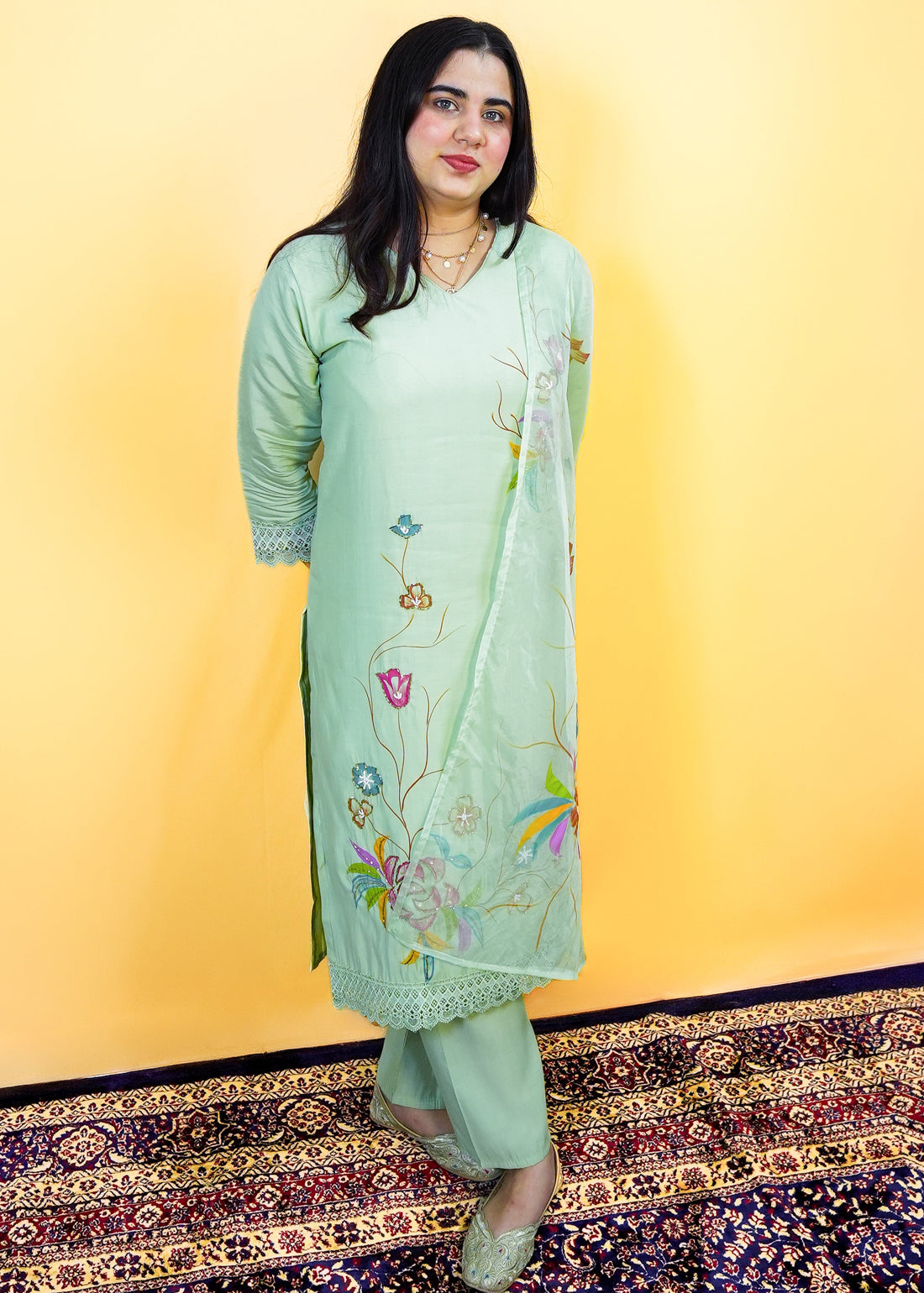 Woman wearing a light green embroidered outfit against a yellow background