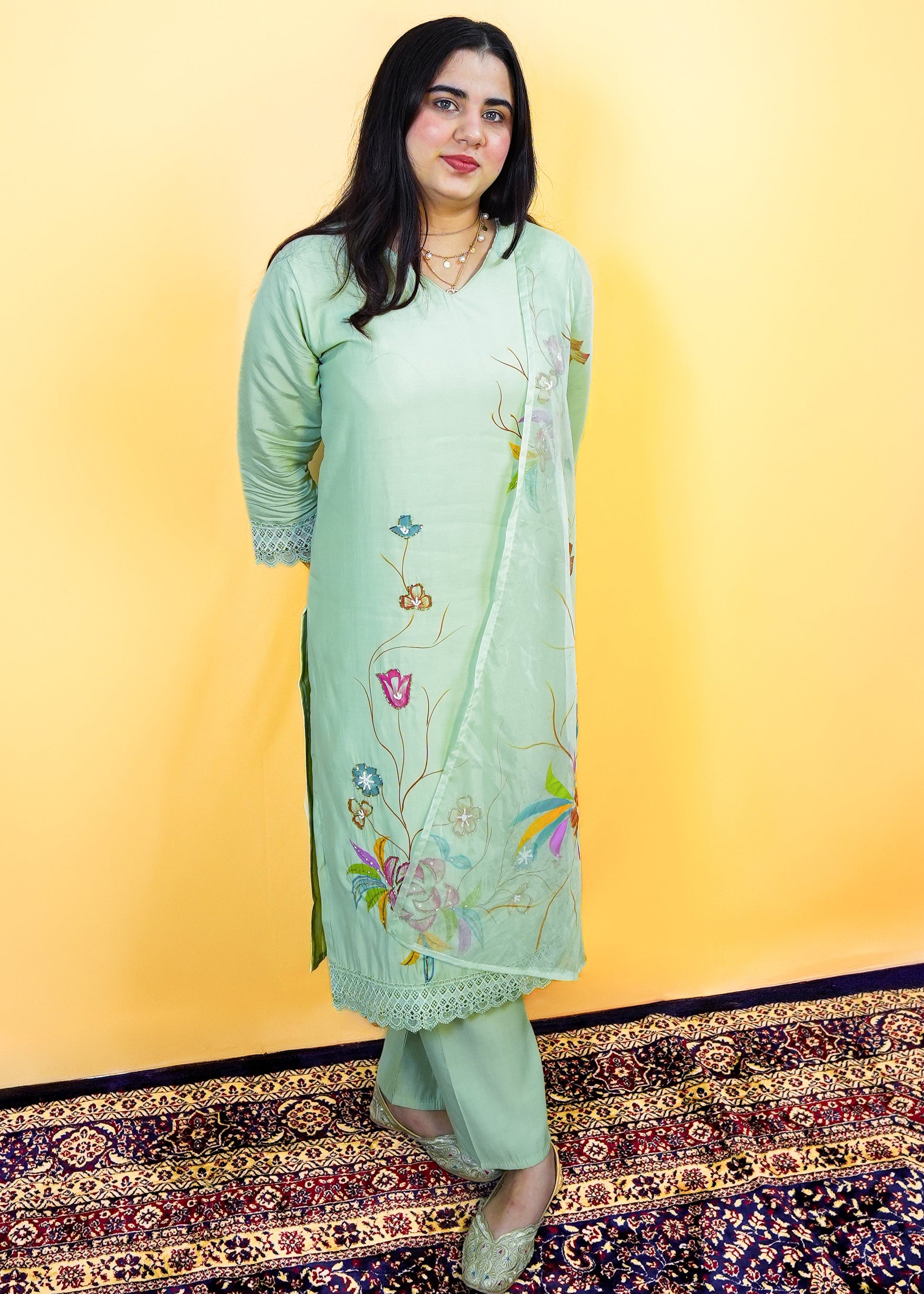 Woman wearing a light green traditional outfit with floral patterns on a yellow background