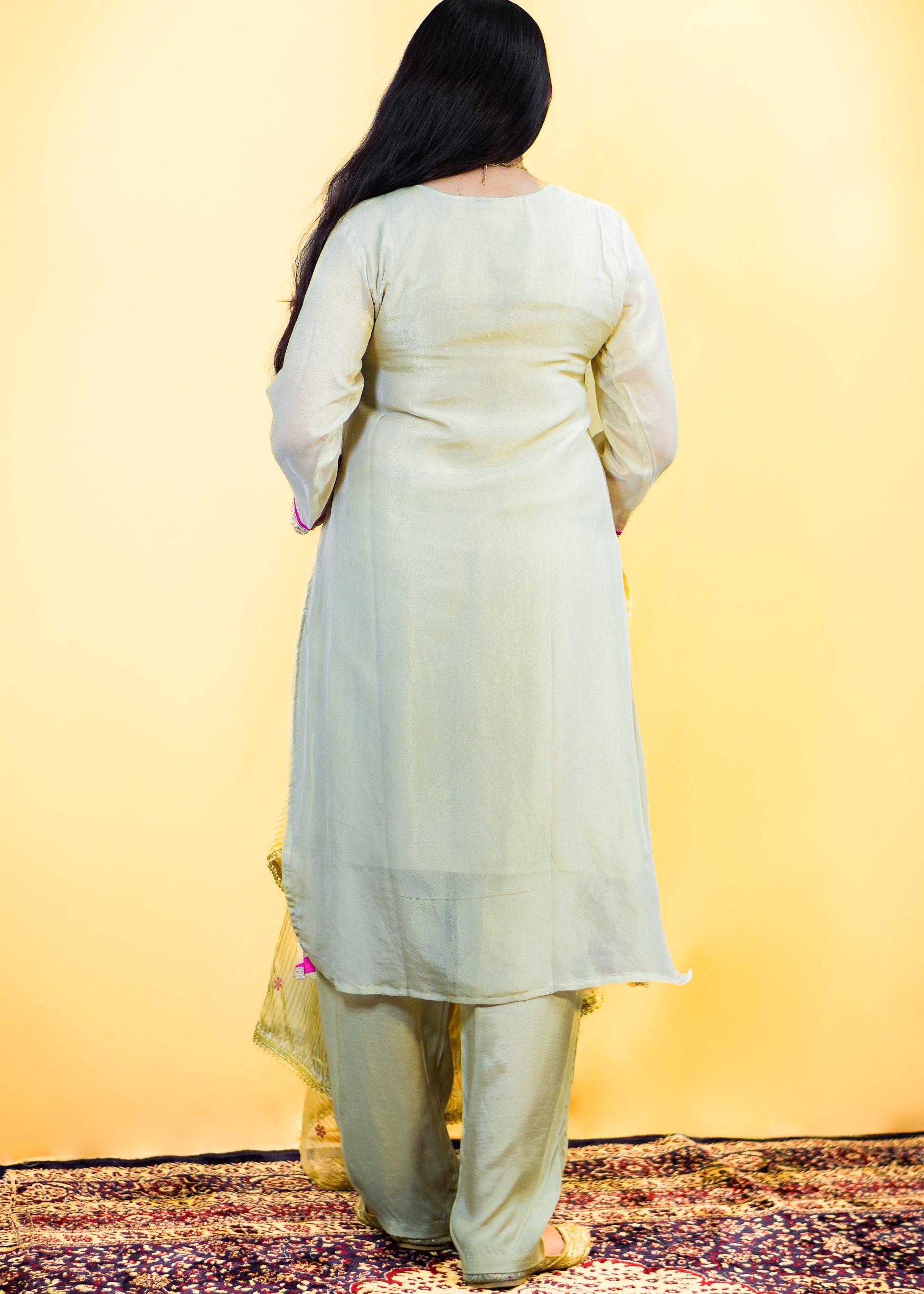 Person wearing a light green traditional outfit with a yellow background
