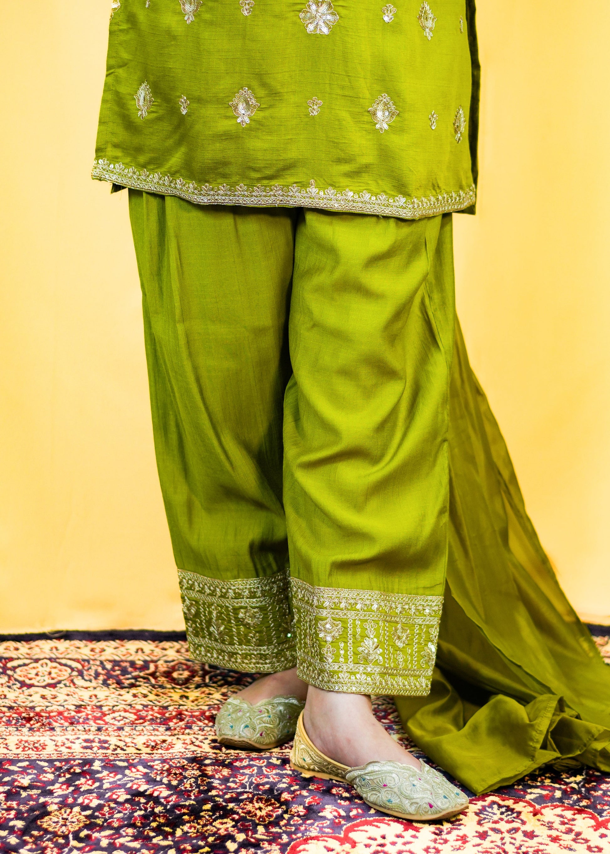 Green traditional outfit with embroidered details on a patterned rug.