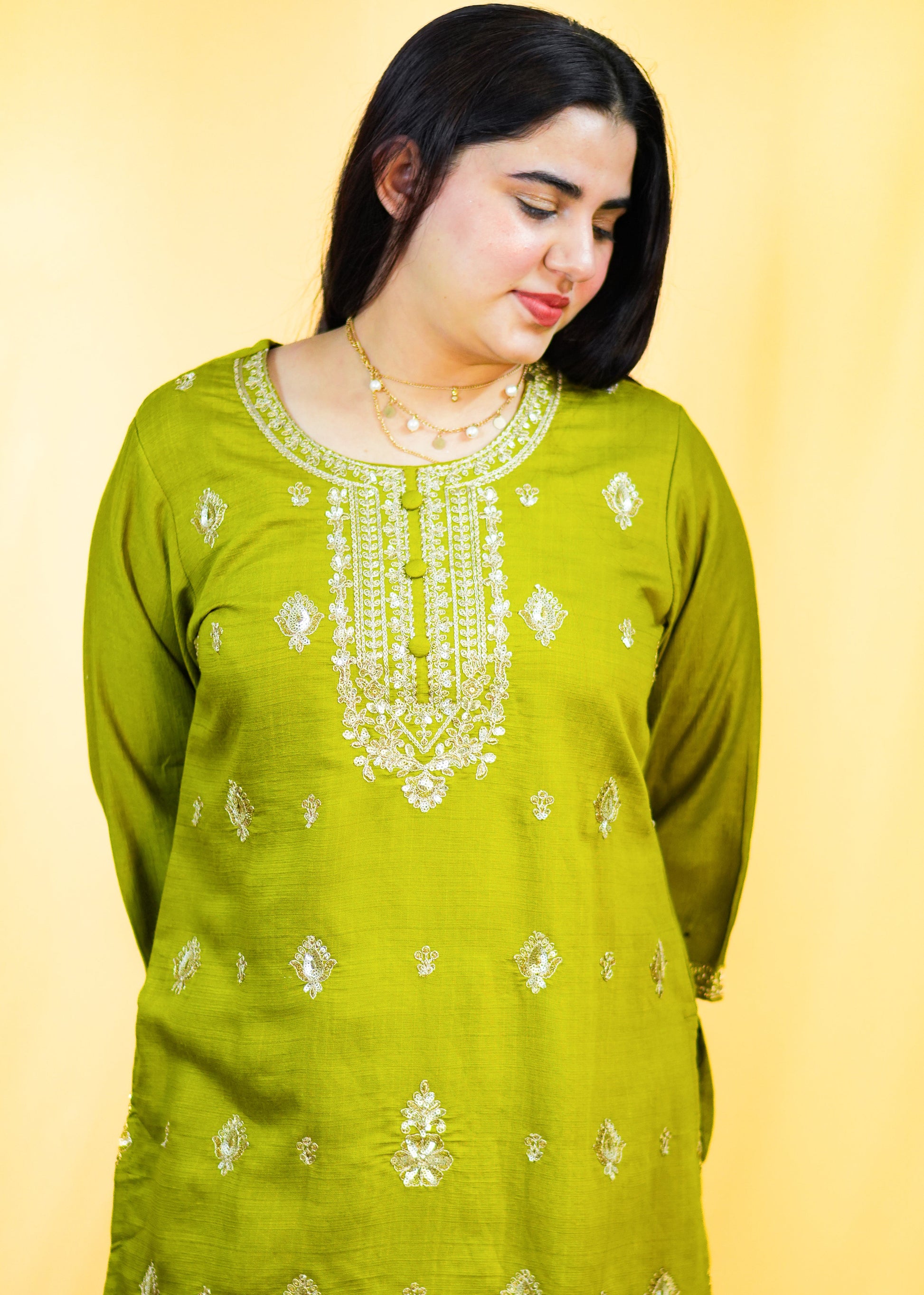 Woman wearing a green embroidered traditional outfit on a yellow background