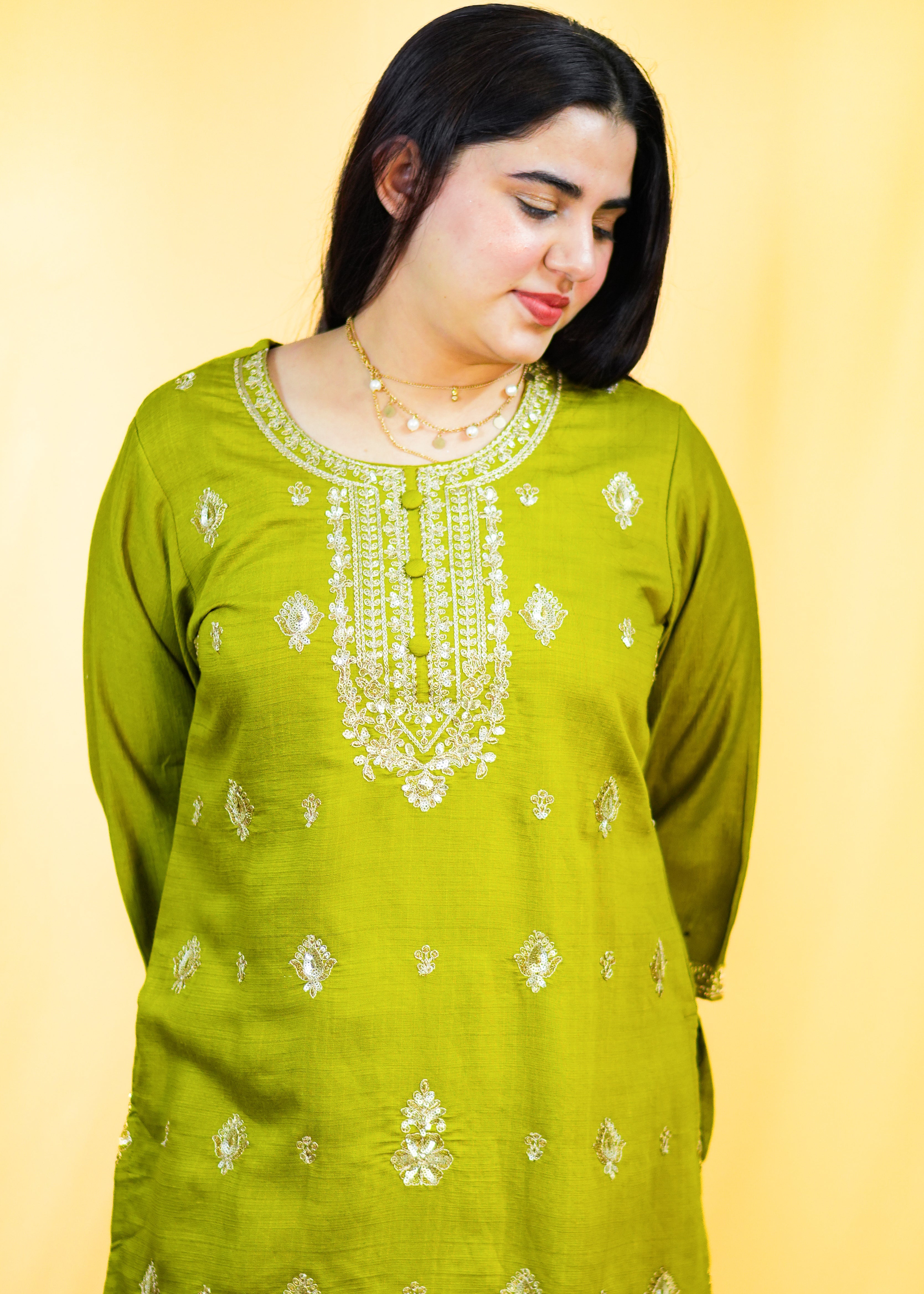 Woman wearing a green embroidered traditional outfit on a yellow background