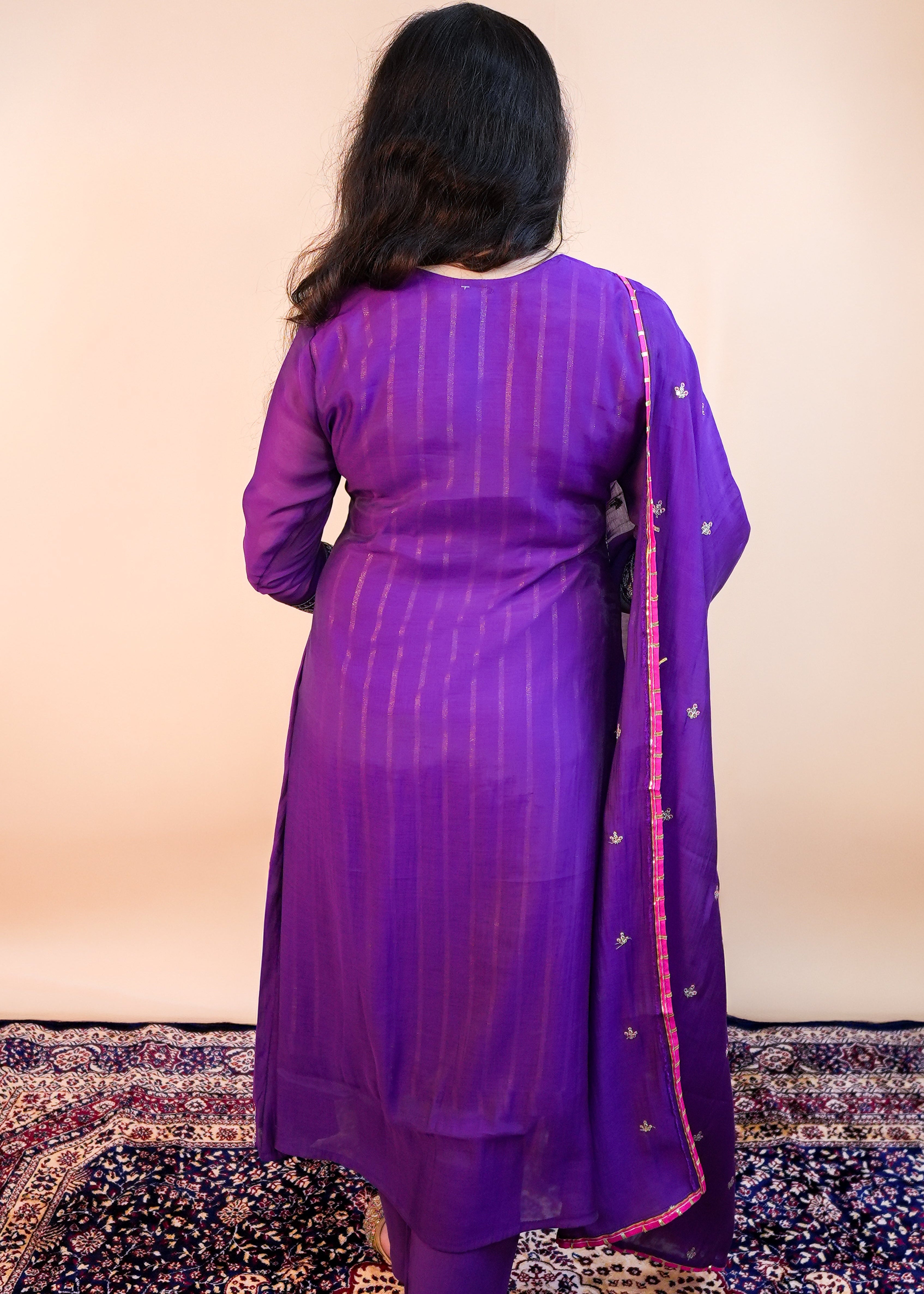 Person wearing a purple traditional outfit with a matching dupatta on a patterned rug.
