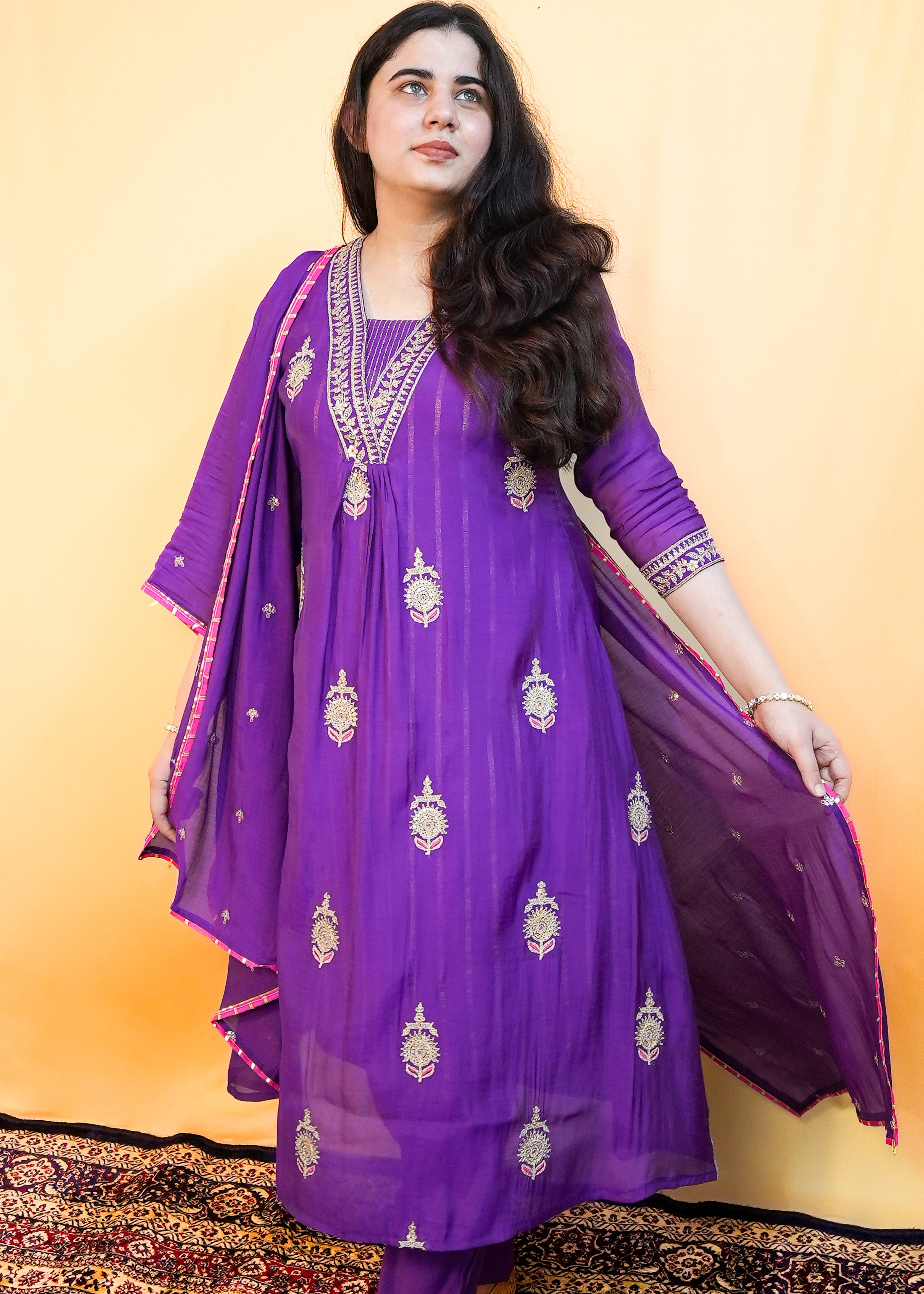 Woman wearing a purple traditional outfit with gold embroidery against a yellow background