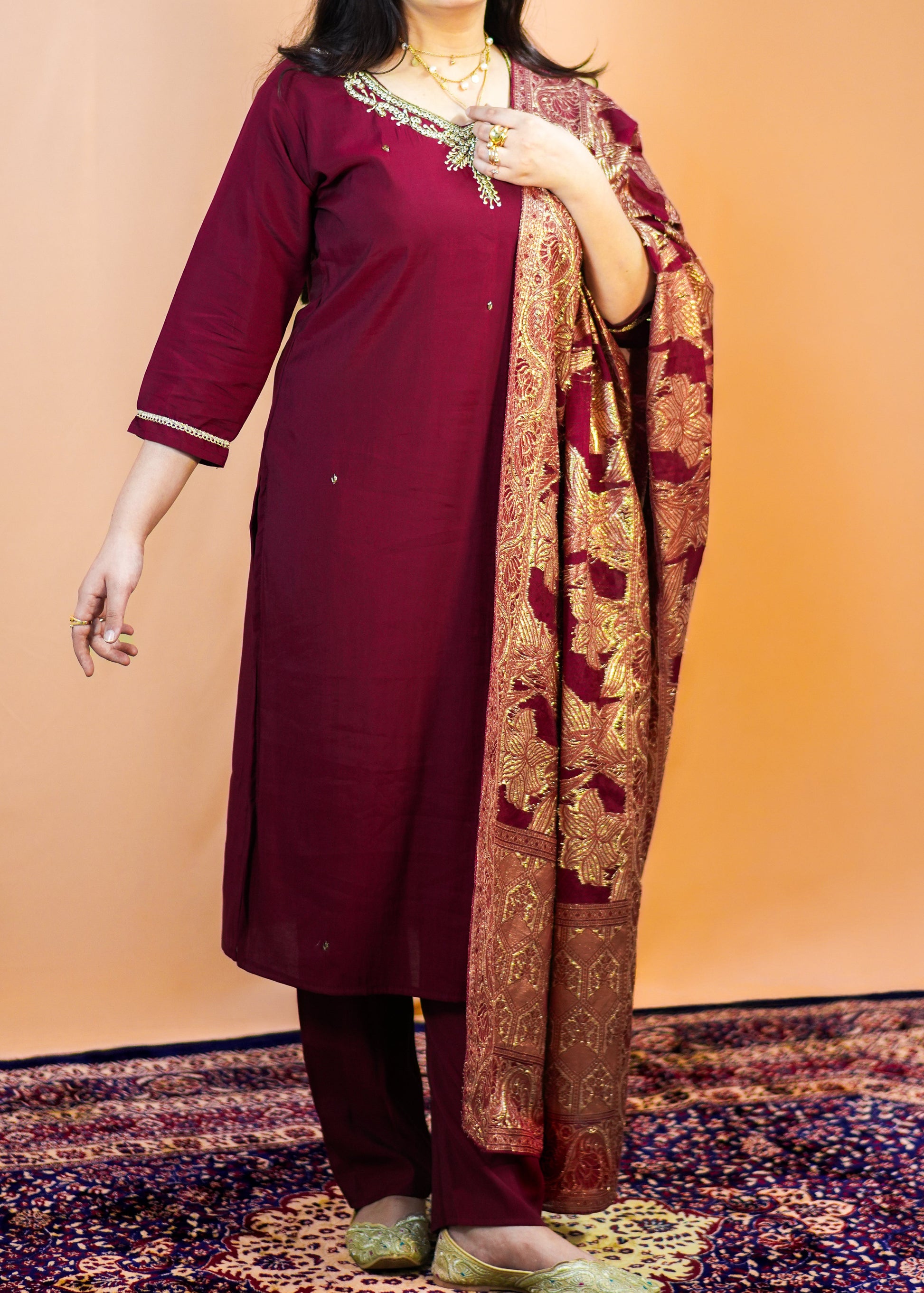 Woman in a maroon traditional outfit with a patterned scarf against an orange background